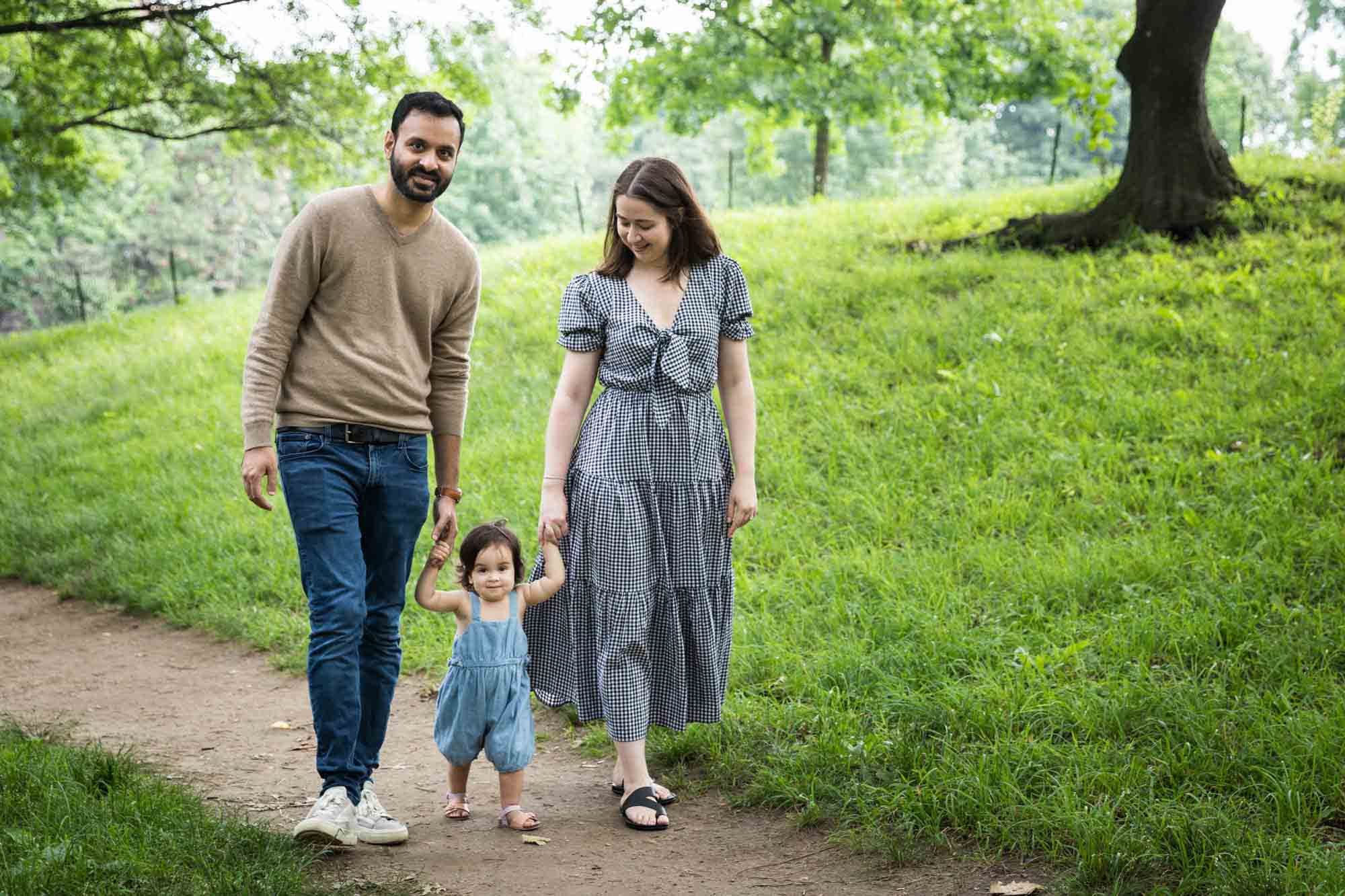 Parents walking down pathway holding hands of toddler during a Fort Green Park family photo shoot