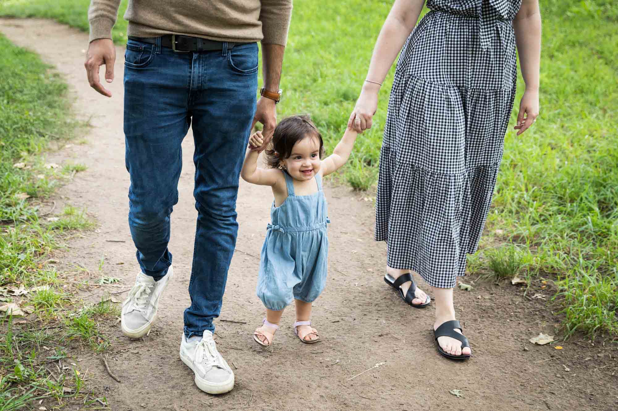 Toddler holding hands of parents while walking during a Fort Green Park family photo shoot