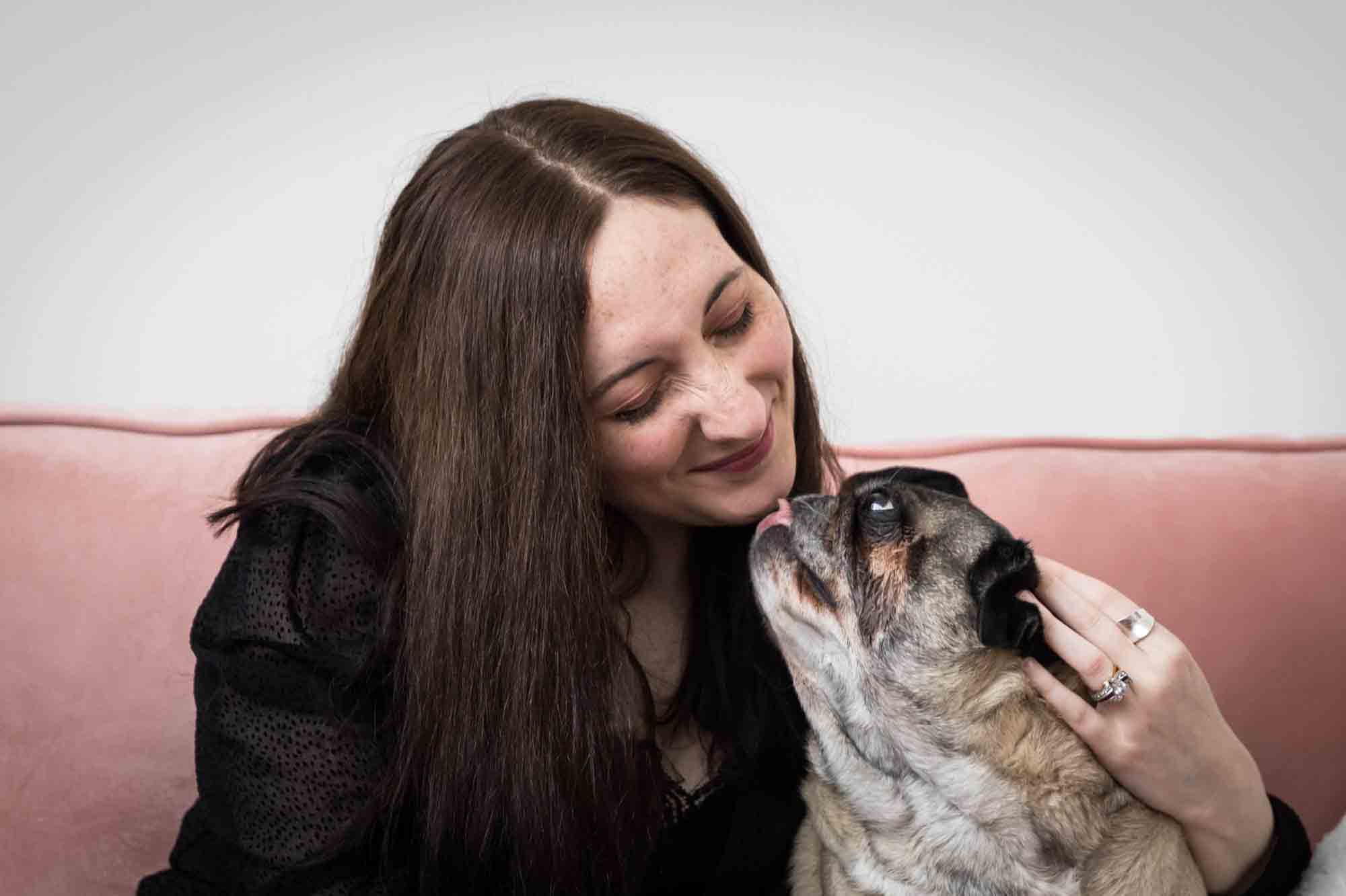 Author Jiordan Castle sitting on pink couch kissing pug dog