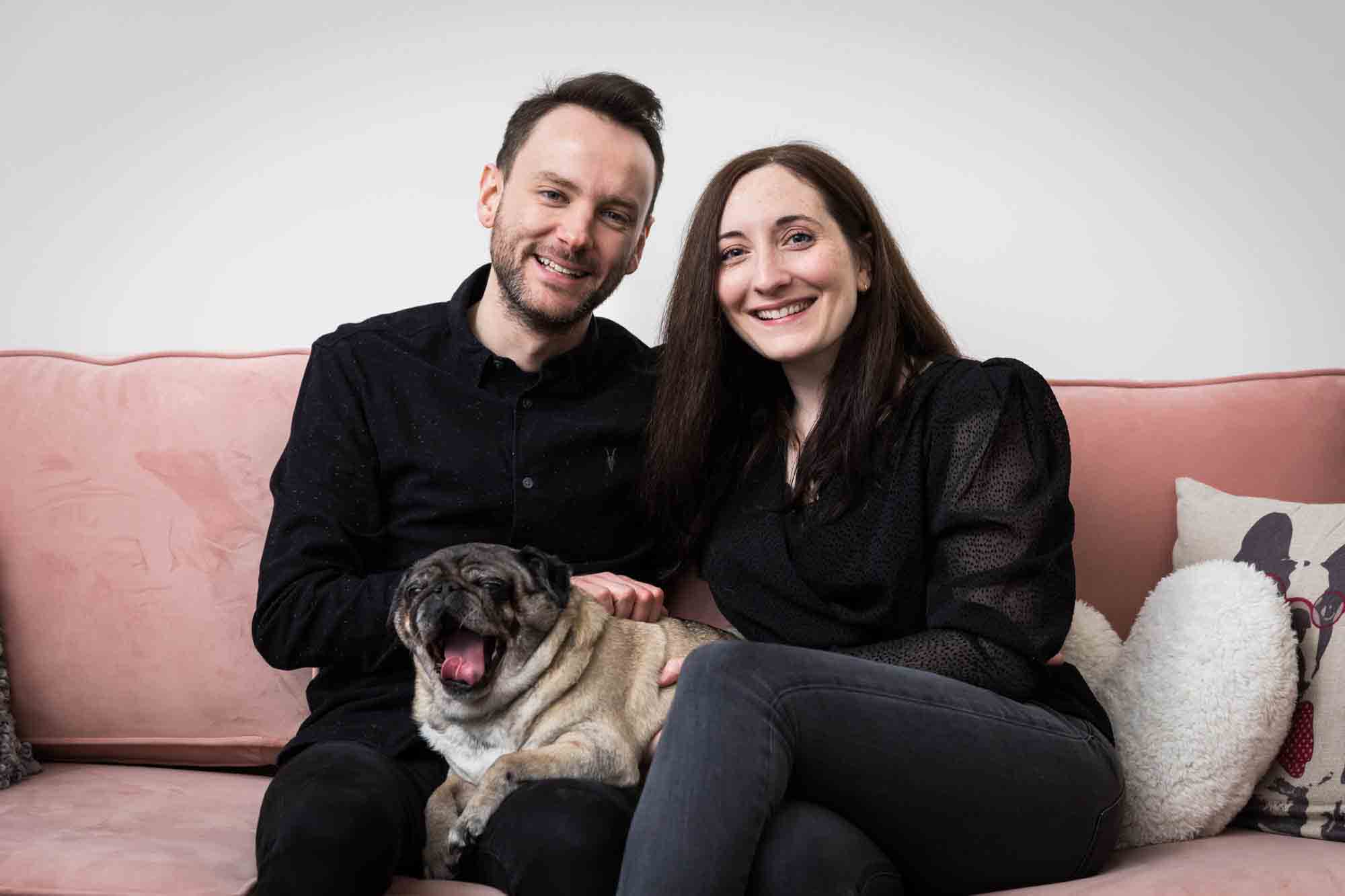 Couple with pug dog sitting on pink couch