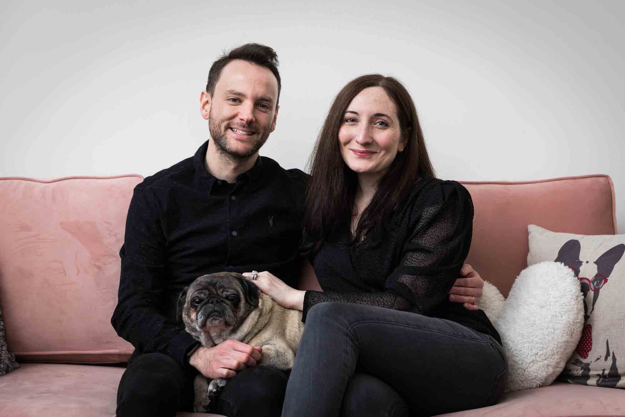 Couple with pug dog sitting on pink couch
