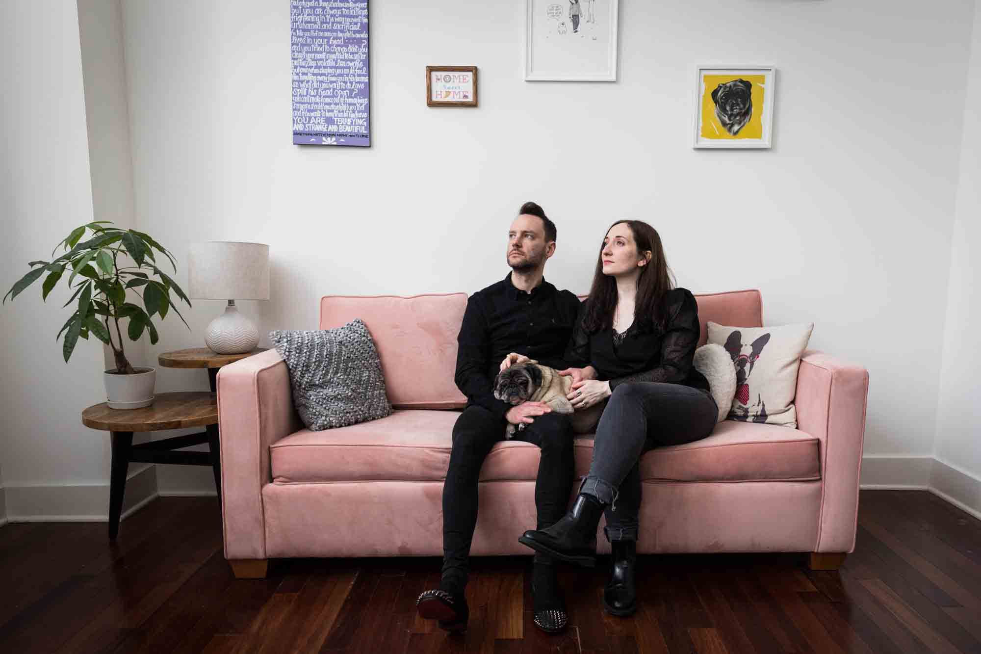 Couple with pug dog sitting on pink couch looking to the side