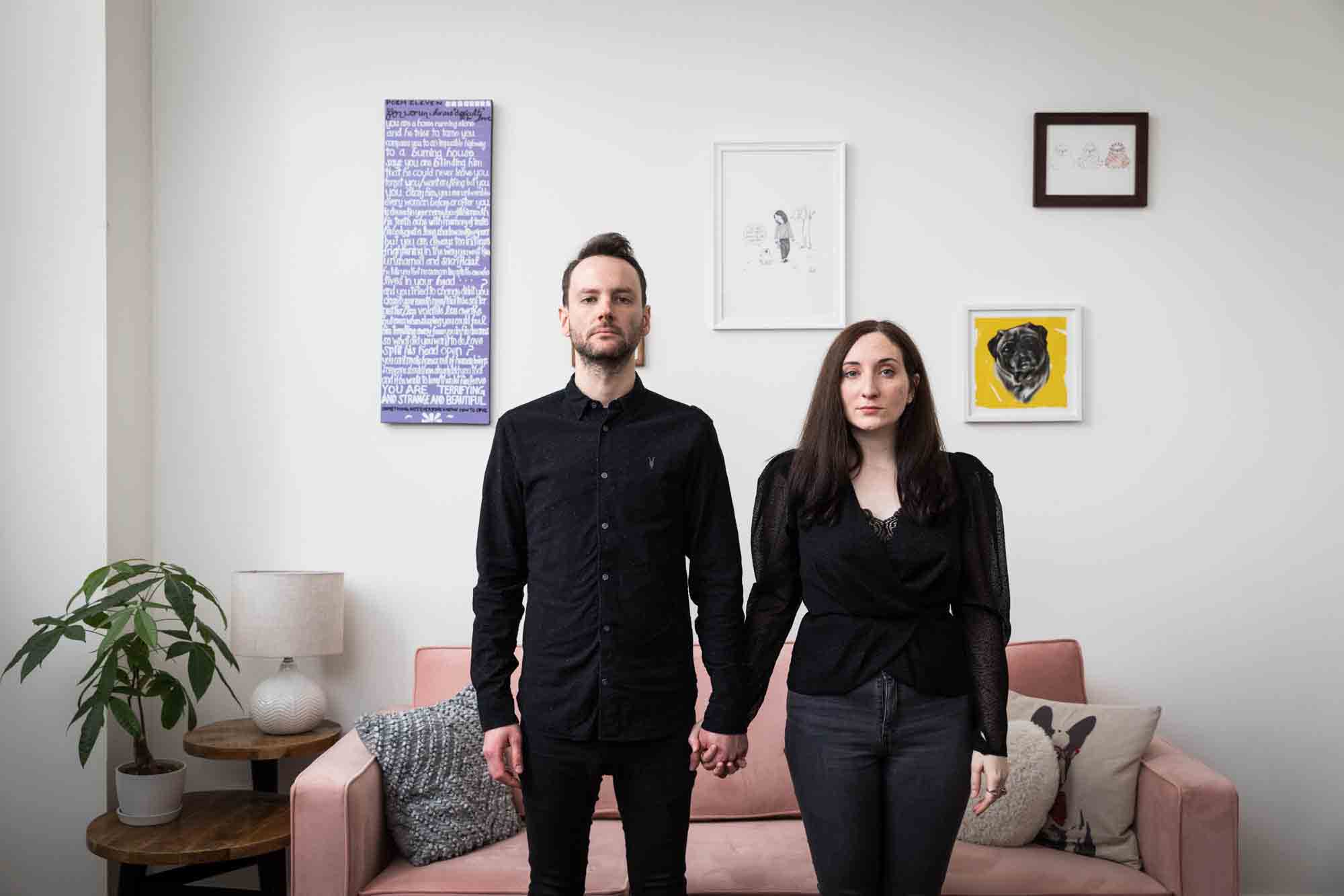 Couple holding hands standing in front of pink couch
