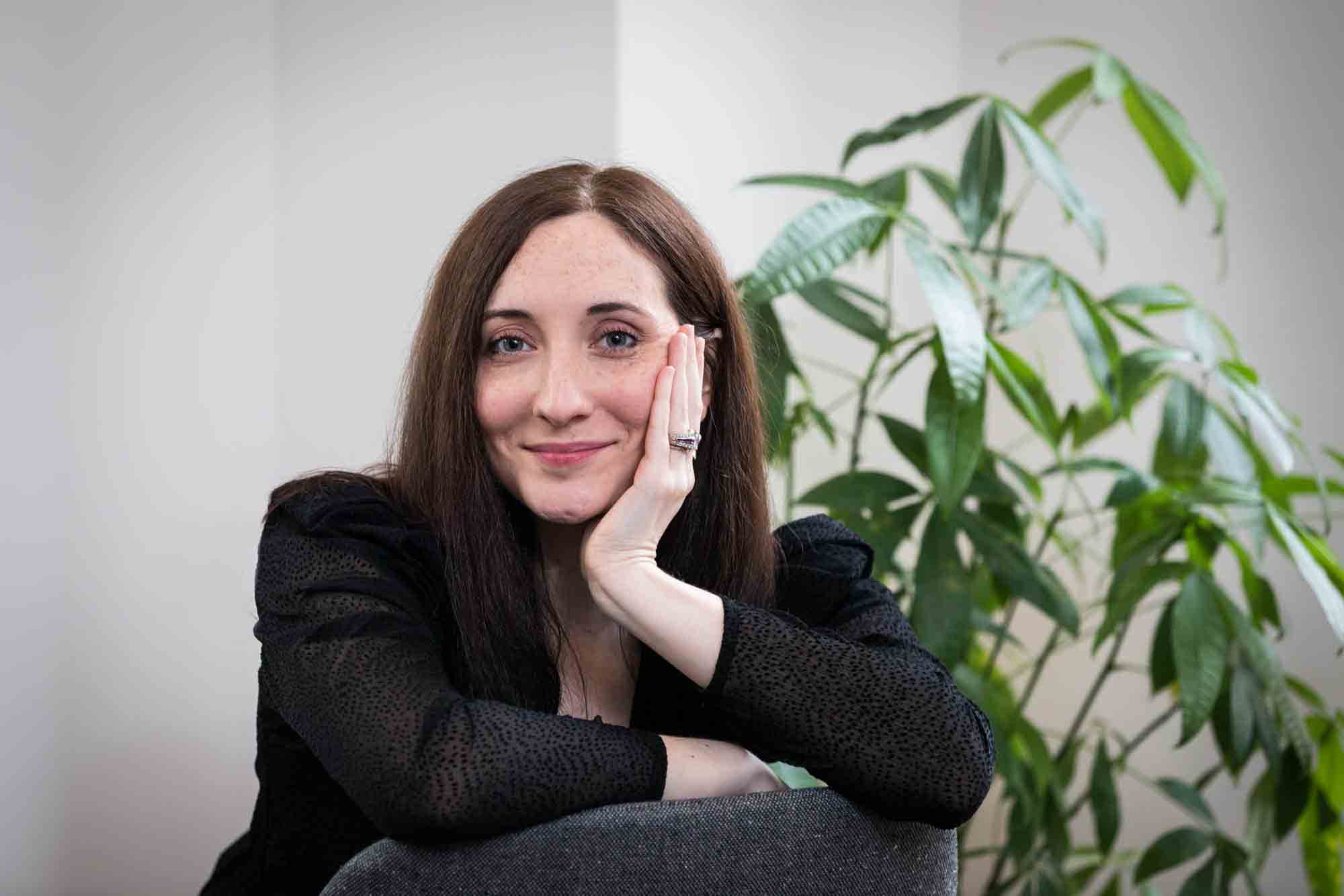 Female author wearing black blouse sitting in chair with plant for an article on professional headshot tips