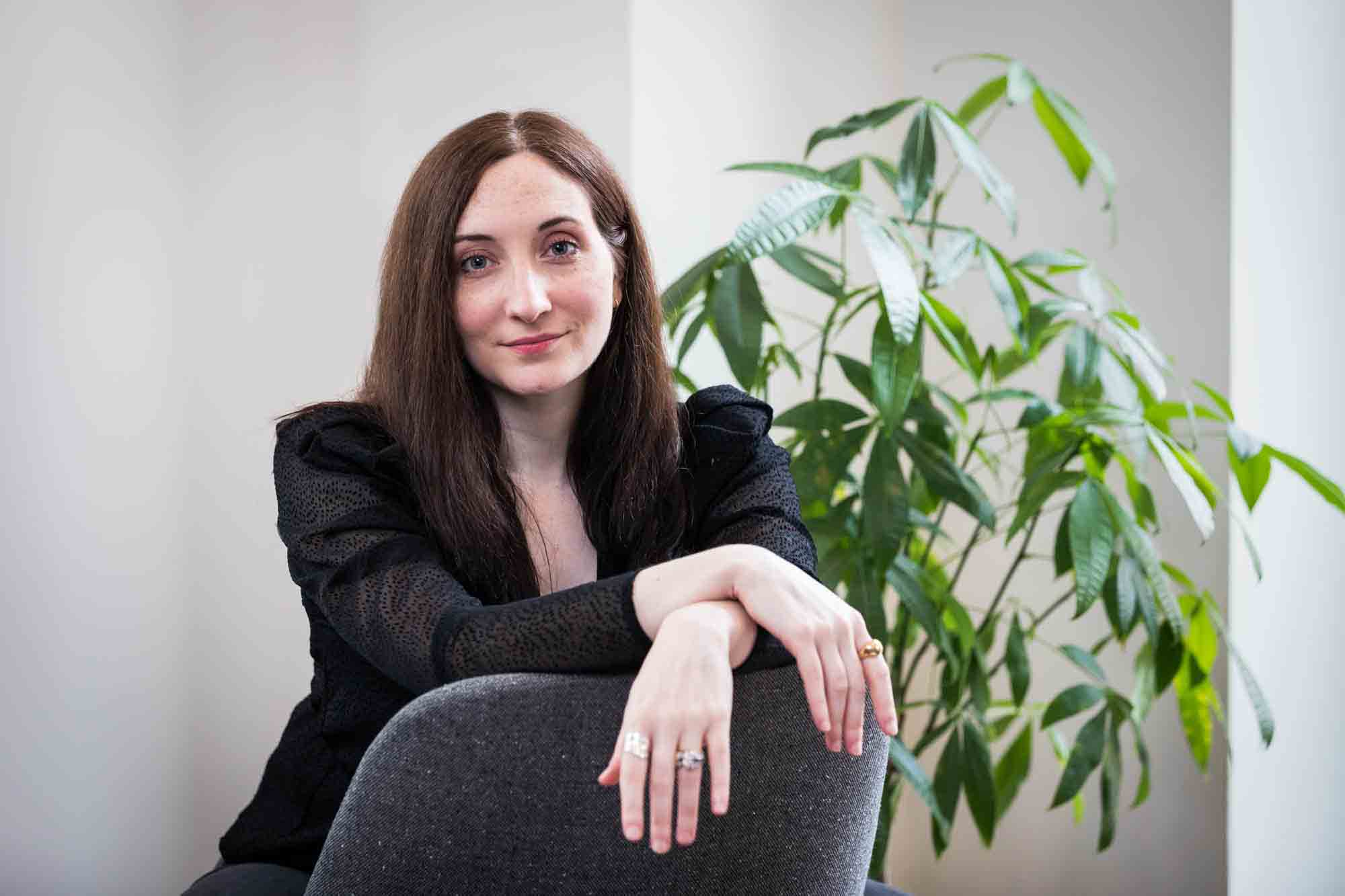 Female author wearing black blouse sitting in chair with plant for an article on professional headshot tips