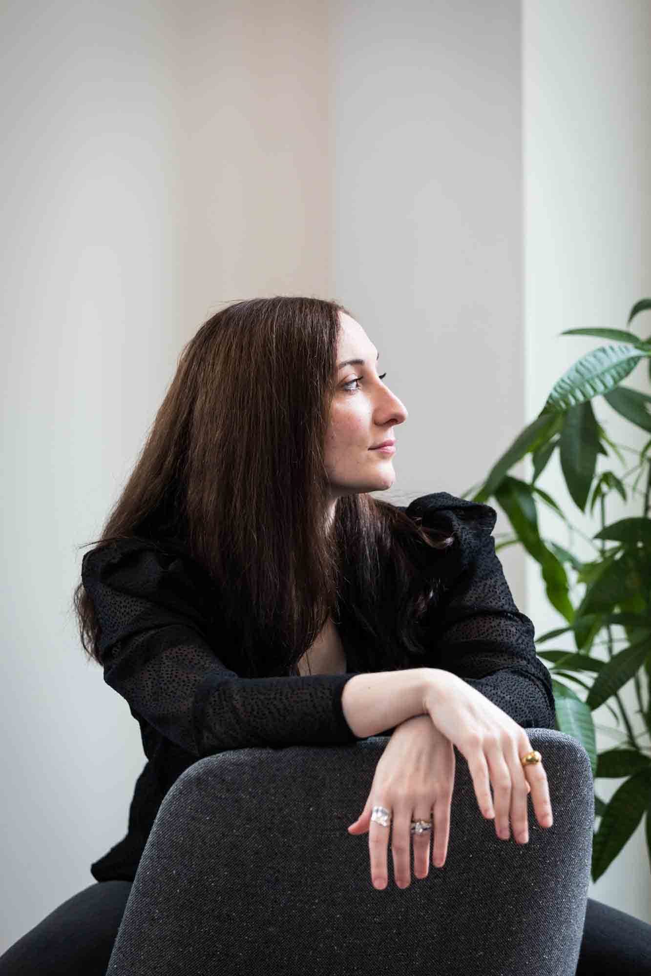 Female author wearing black blouse sitting in chair with plant for an article on professional headshot tips