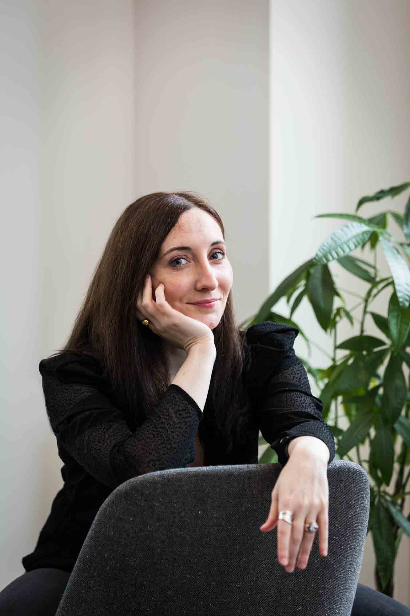Female author wearing black blouse sitting in chair with plant for an article on professional headshot tips