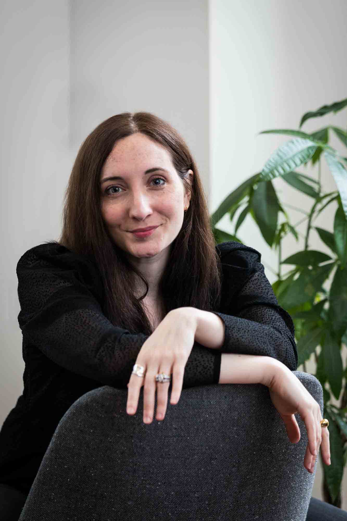 Female author wearing black blouse sitting in chair with plant for an article on professional headshot tips