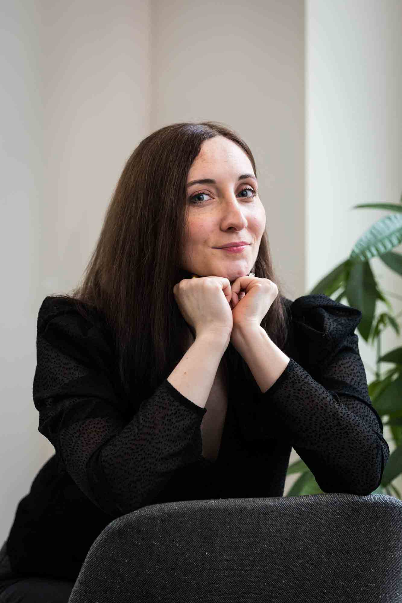 Female author wearing black blouse sitting in chair with plant for an article on professional headshot tips