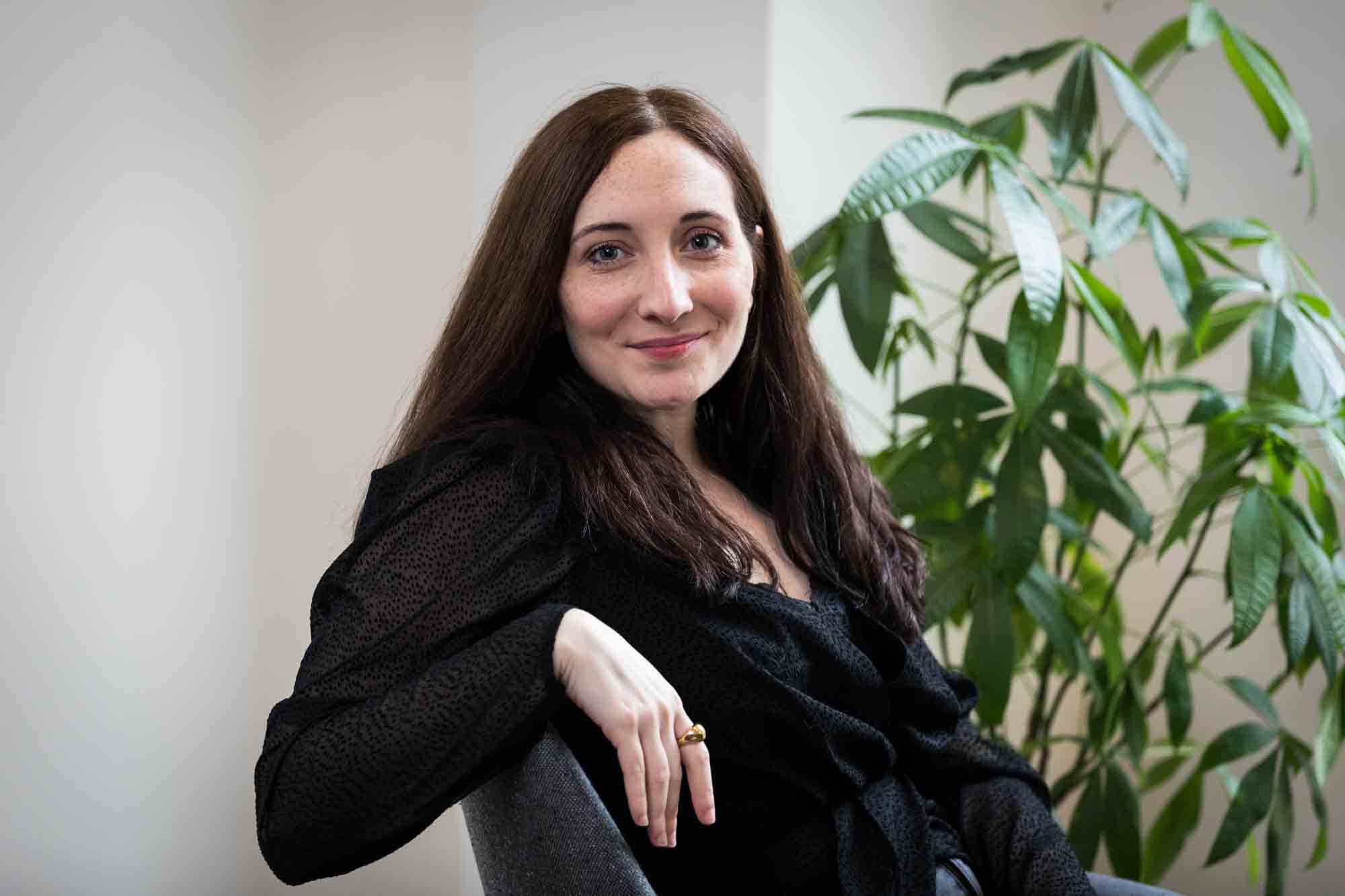 Female author wearing black blouse sitting in chair with plant for an article on professional headshot tips