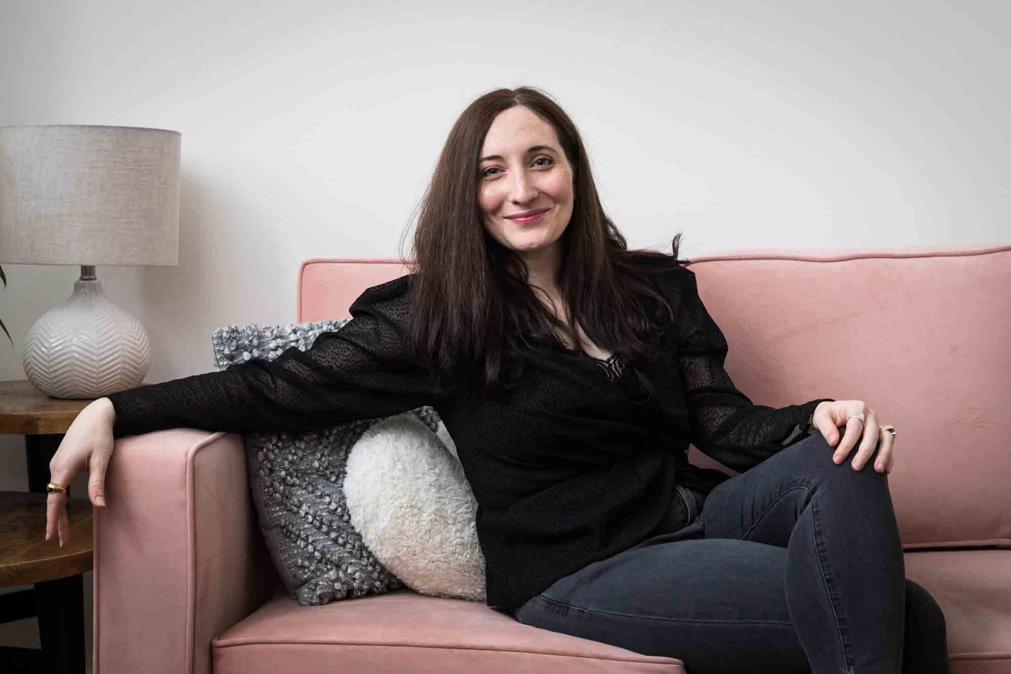 Woman wearing black blouse and black jeans sitting on pink couch 