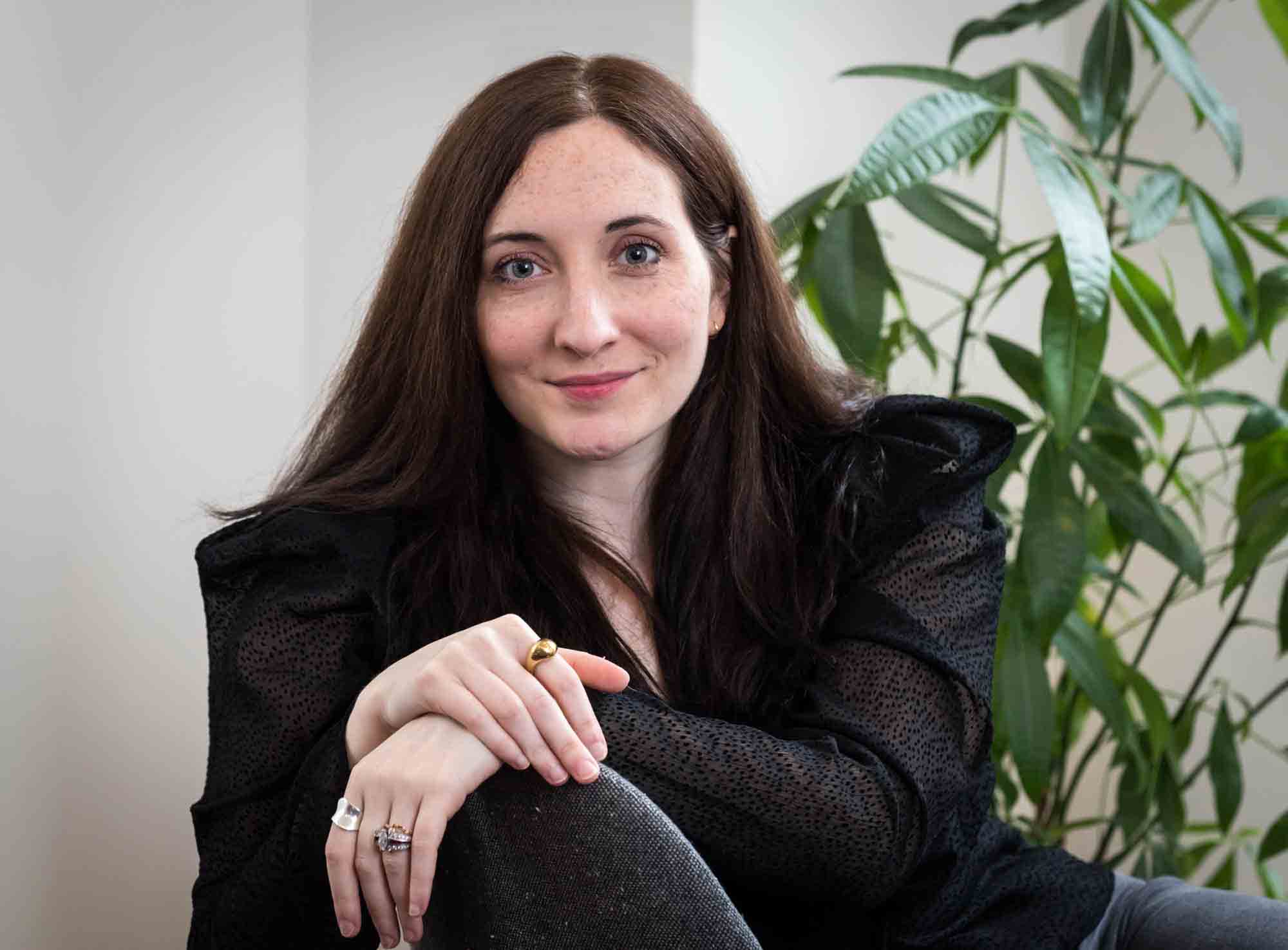 Female author wearing black blouse sitting in chair with plant for an article on professional headshot tips