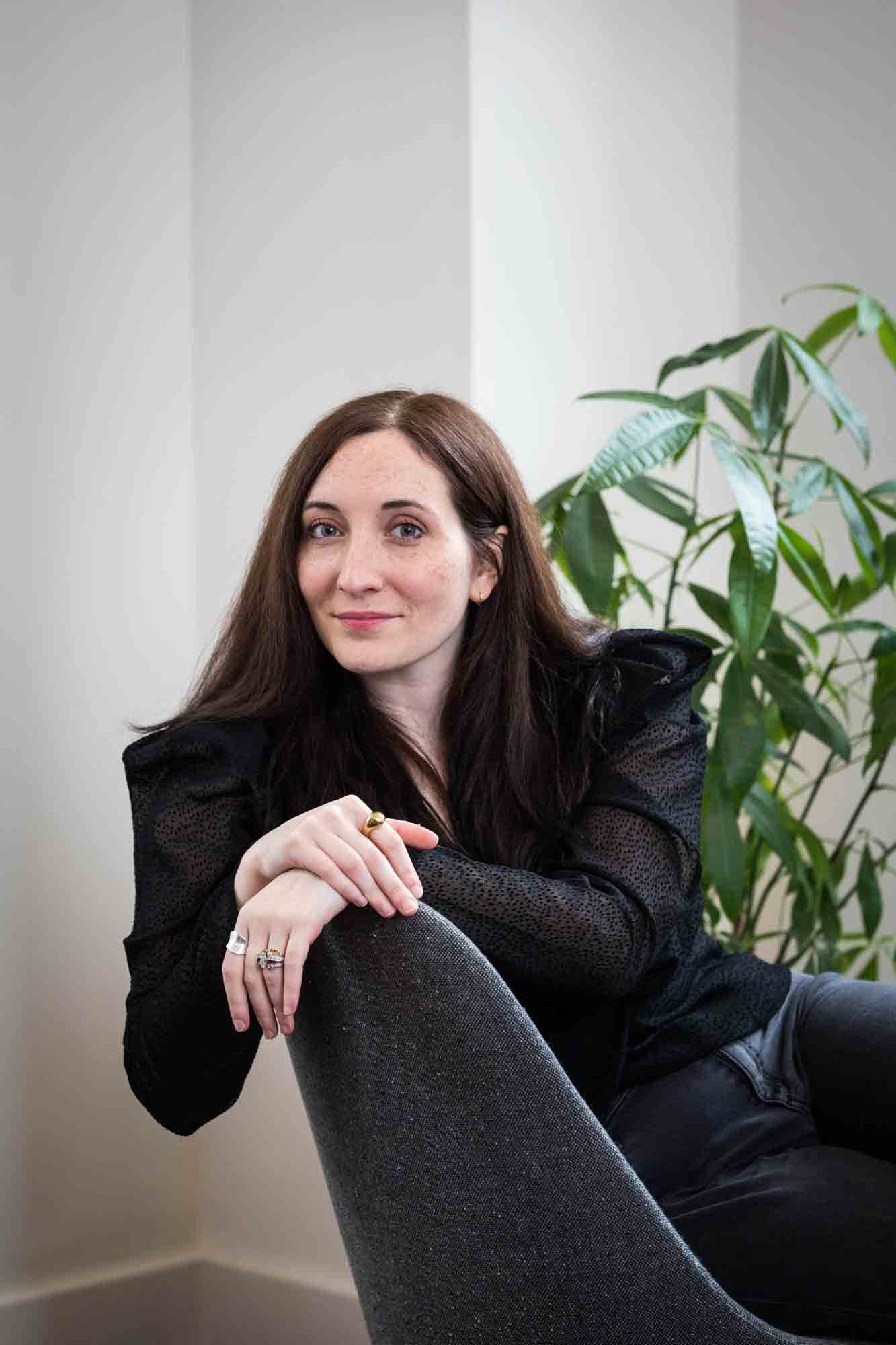 Female author wearing black blouse sitting in chair with plant for an article on professional headshot tips