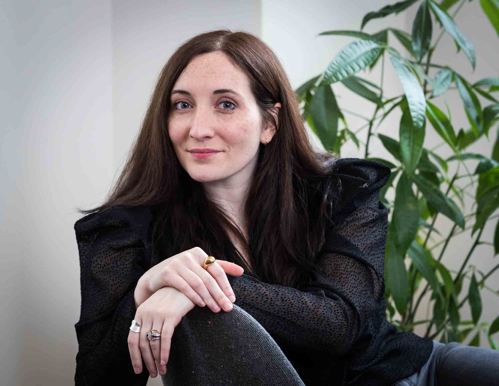 Female author wearing black blouse sitting in chair with plant for an article on professional headshot tips