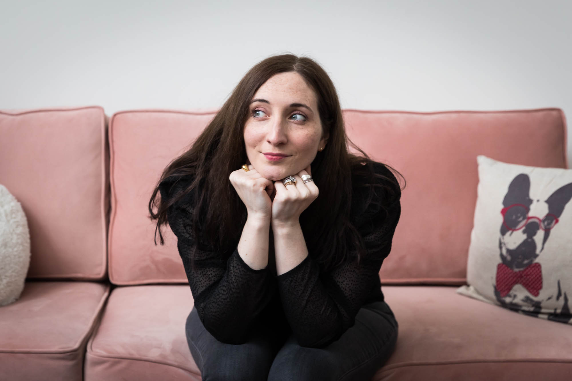 Headshot of female author with hands under chin on pink couch for an article on professional headshot tips