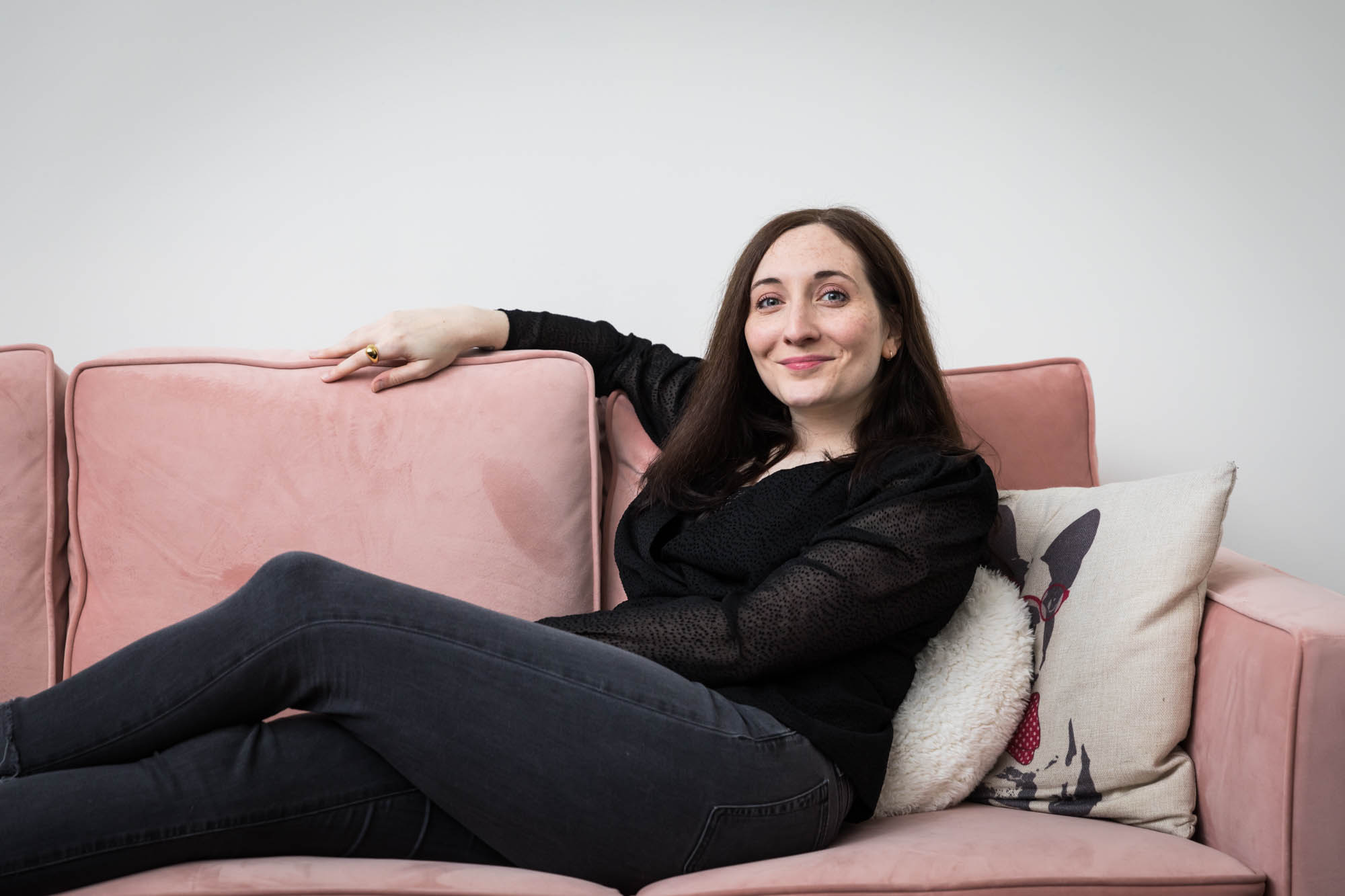Woman wearing black blouse and black jeans sitting on pink couch