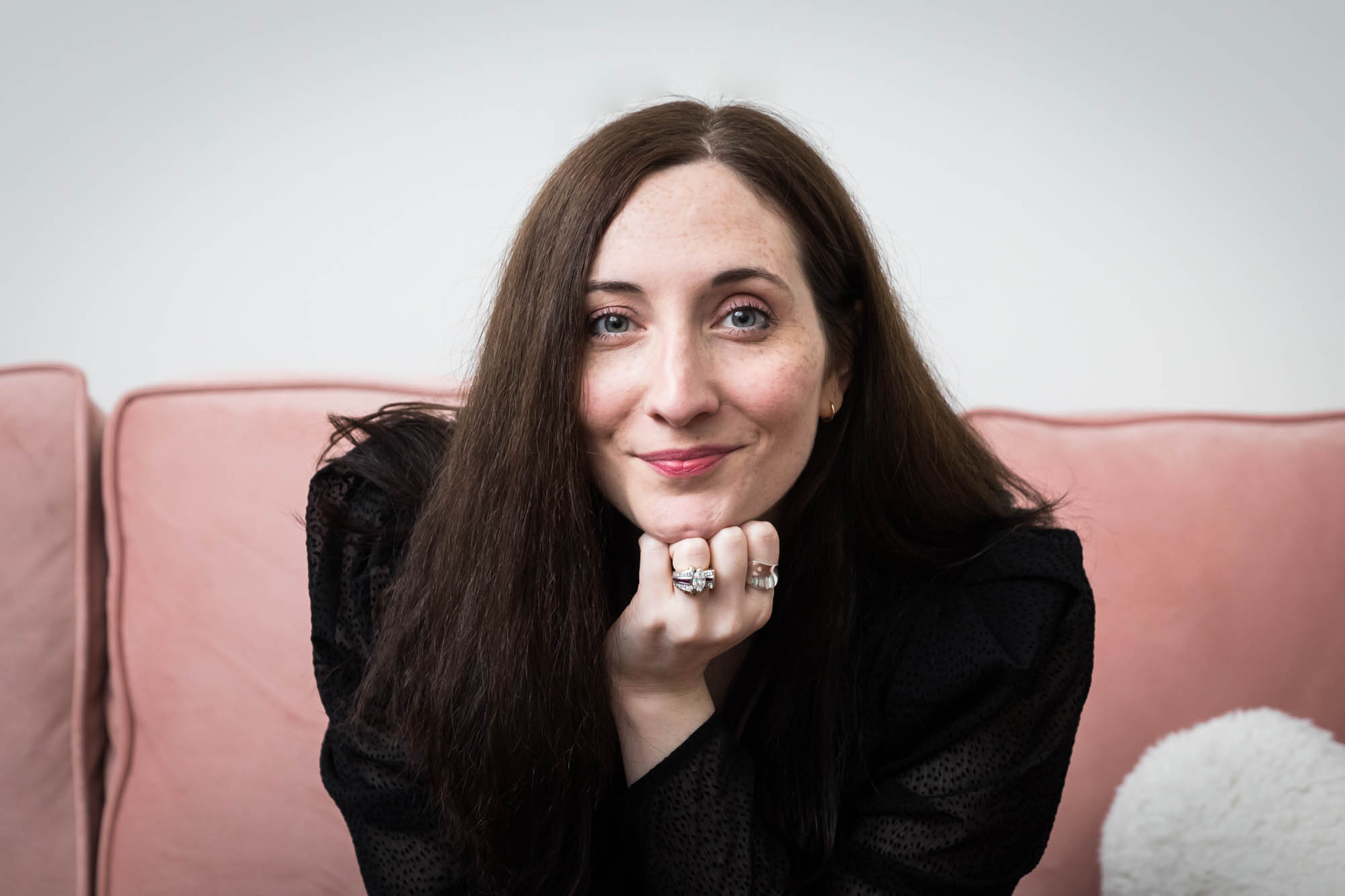 Headshot of female author with hand under chin on pink couch for an article on professional headshot tips