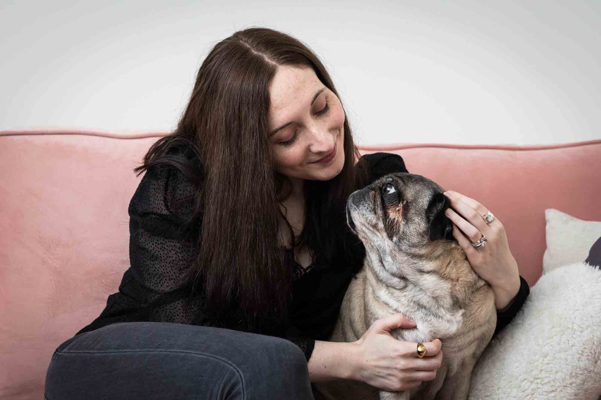 Author Jiordan Castle sitting on pink couch looking down at pug dog