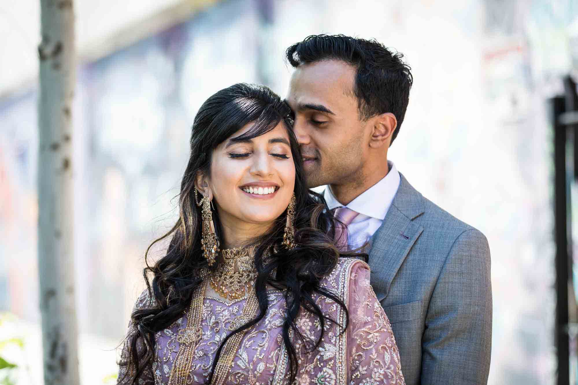Groom kissing Indian bride on the side of the head for article on wedding reception game ideas