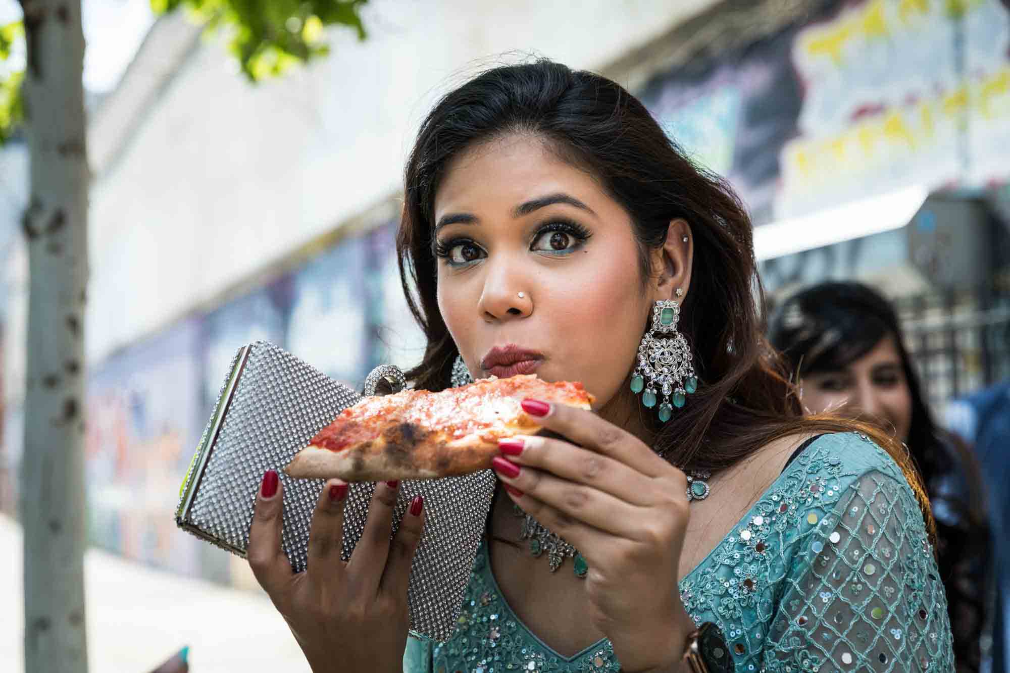 Female Indian guest wearing teal dress eating a piece of pizza