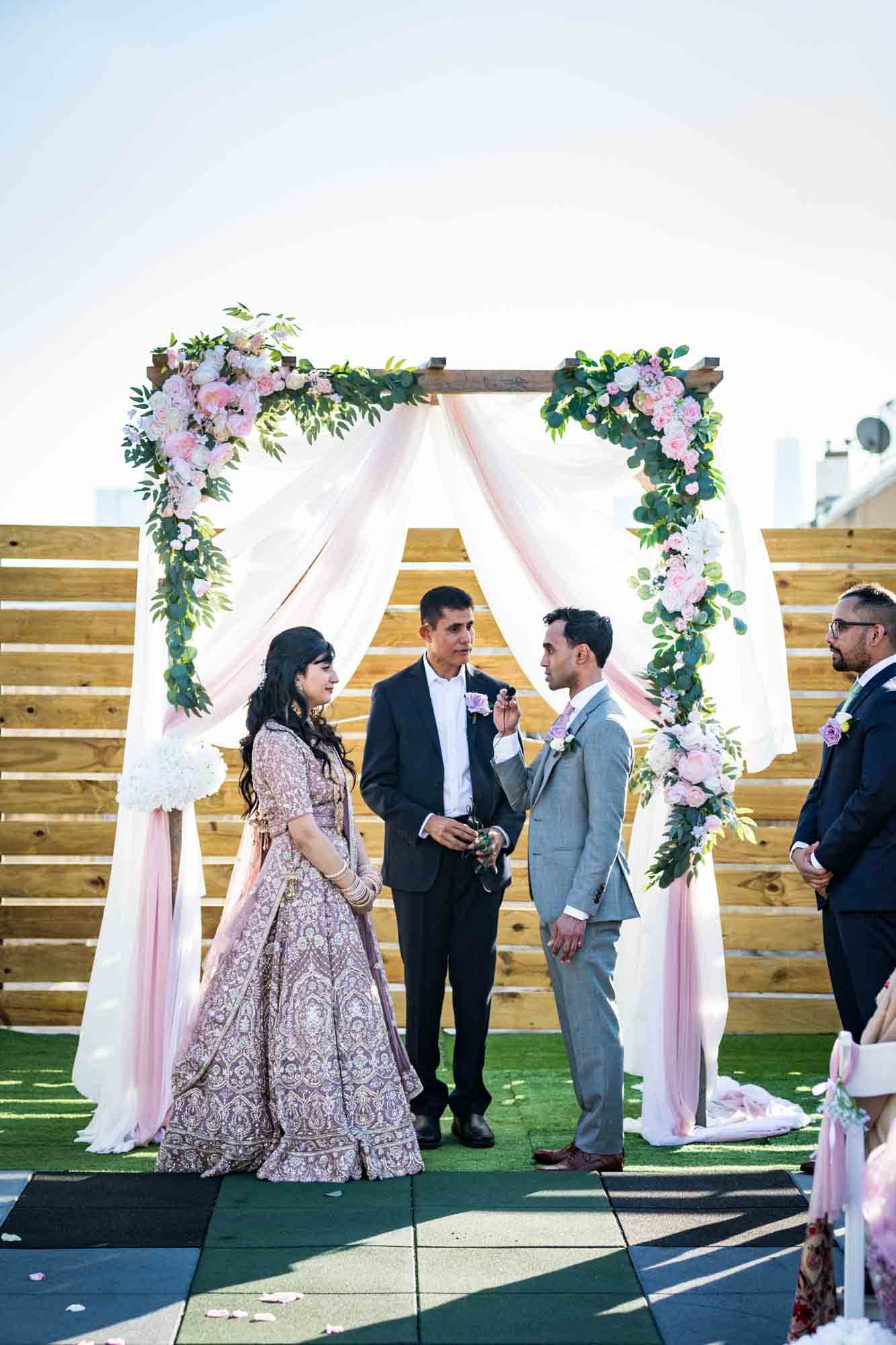 Bride and groom saying vows under floral arch for article on wedding reception game ideas