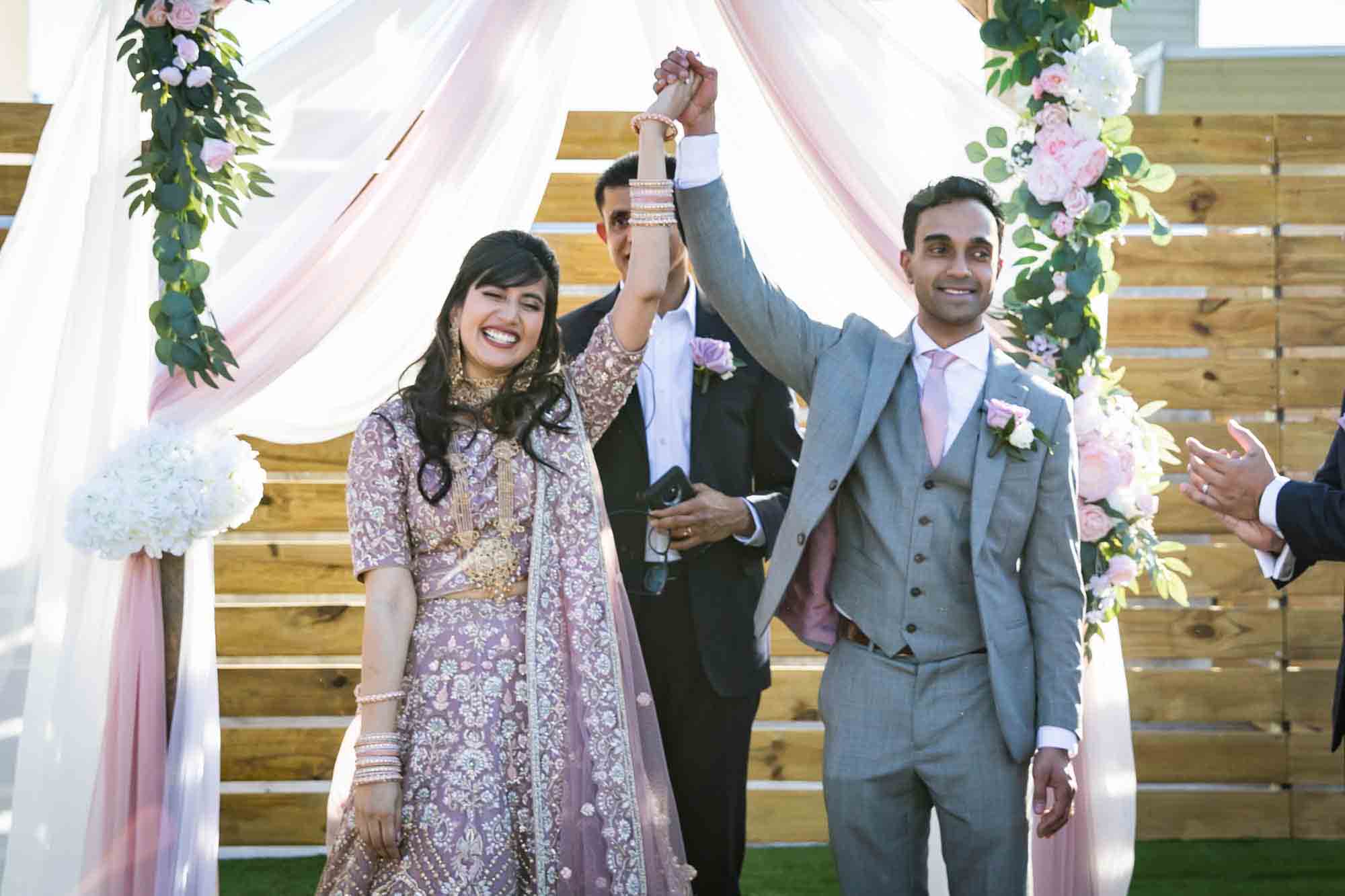 Indian bride and groom raising hand in the air after ceremony for article on wedding reception game ideas