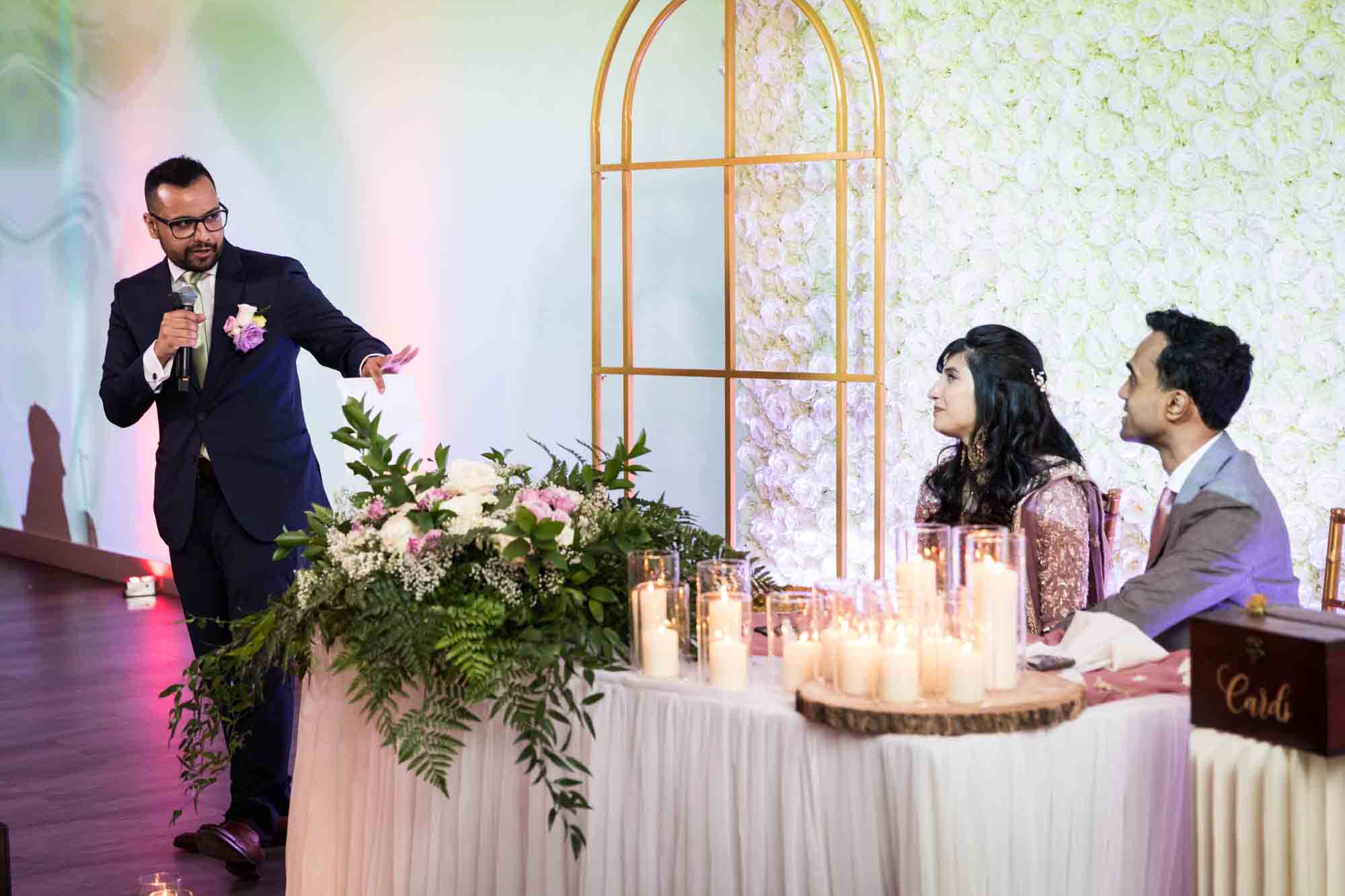 Indian bride and groom listening to man making speech at a Loft Story wedding