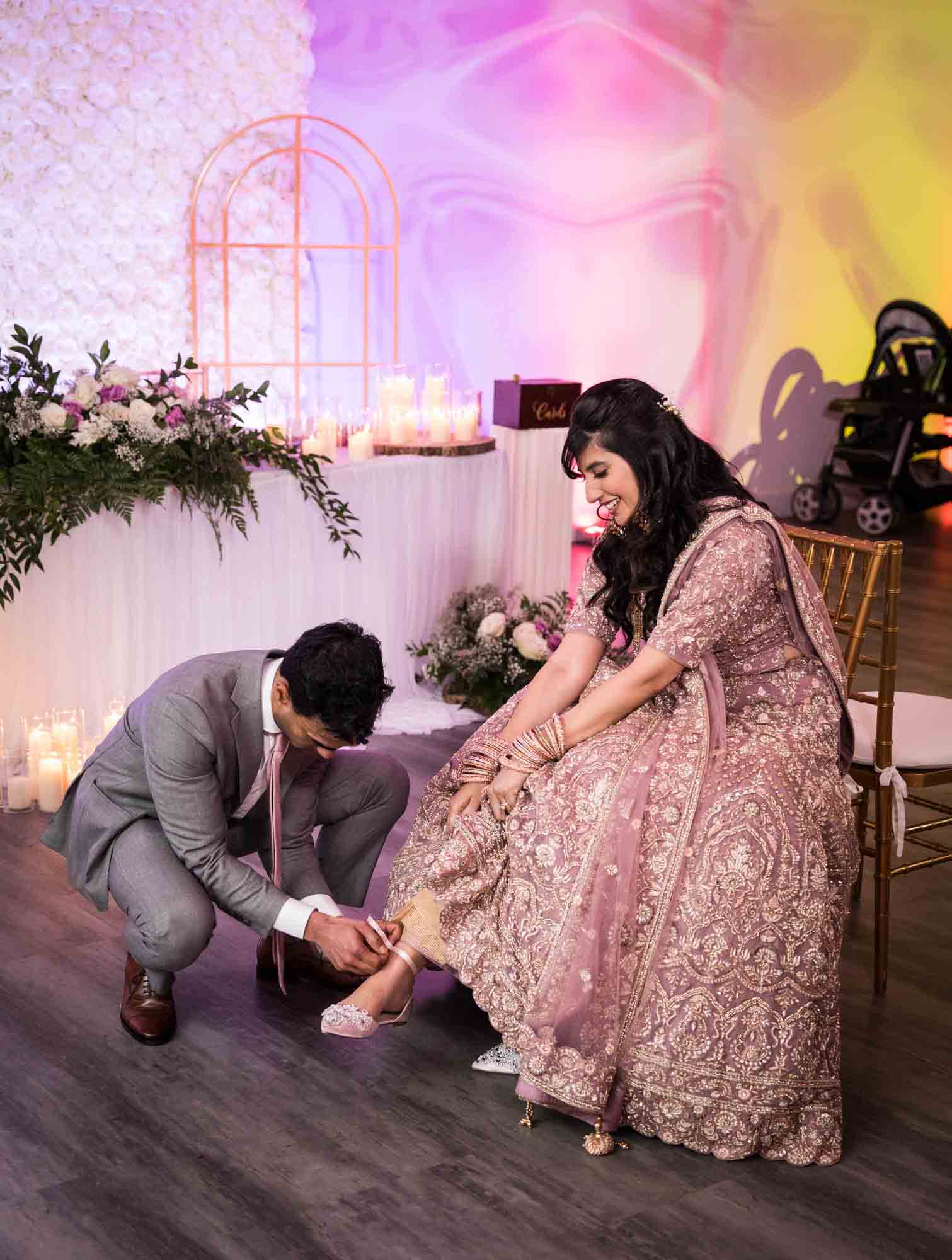 Groom helping Indian bride take off shoe at table at a Loft Story wedding