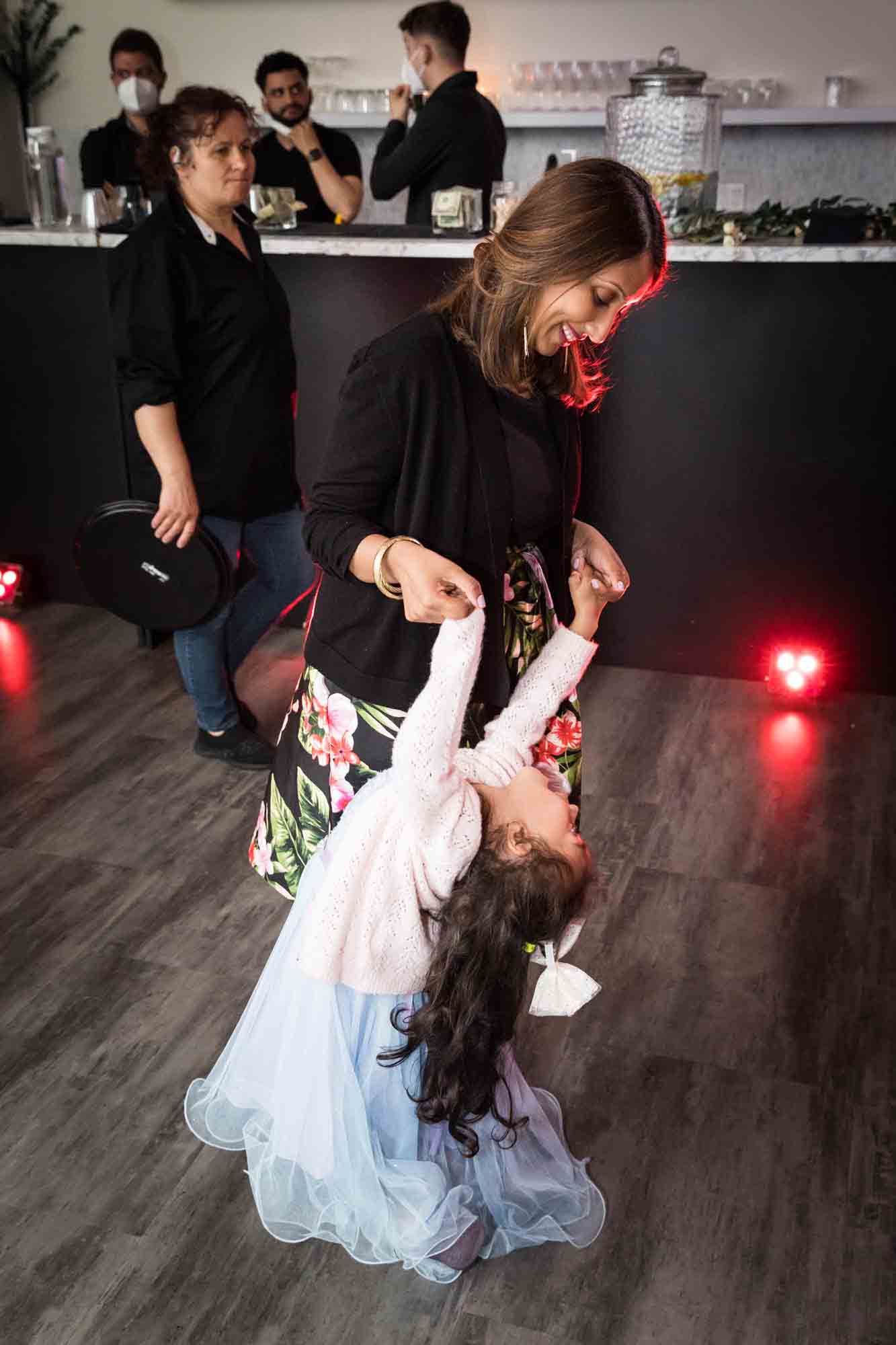 Mother dancing with little girl holding her arms Bride and groom holding up shoes on dance floor for article on wedding reception game ideas