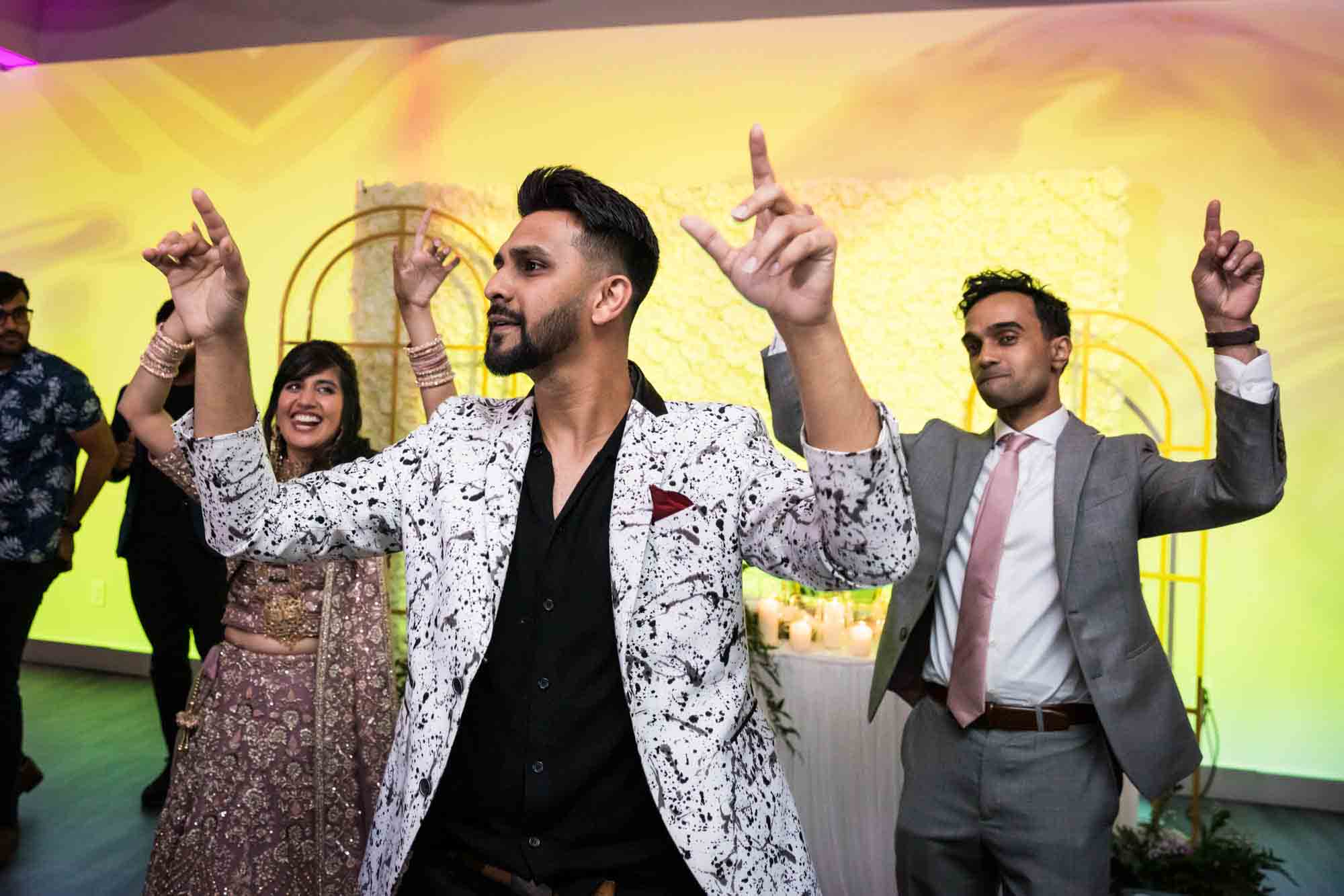 DJ with hands raised leading Indian bride and groom on dance floor at a Loft Story wedding