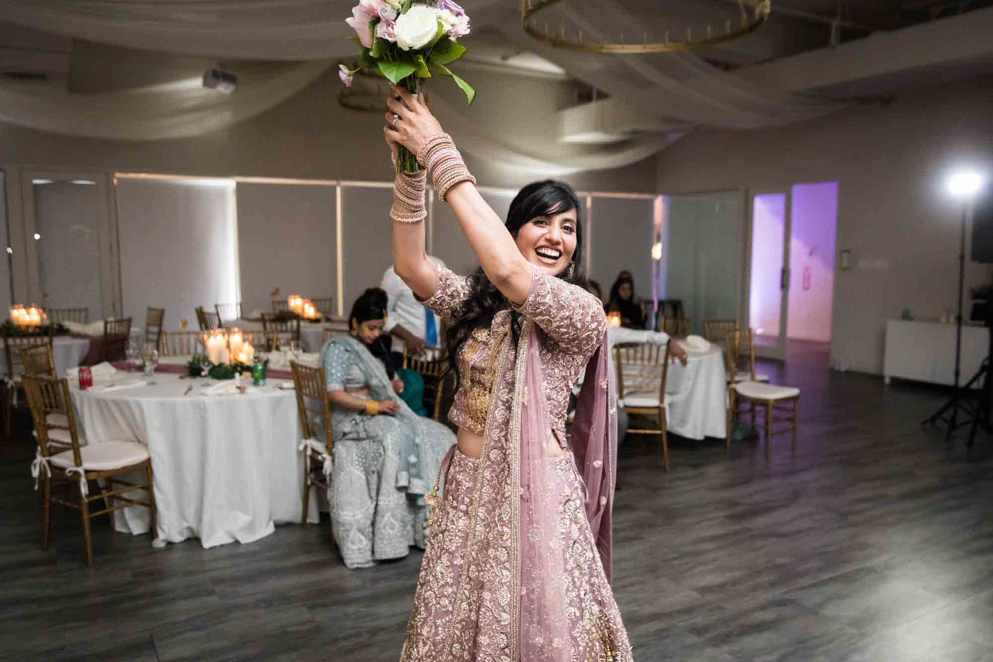 Bride holding up flower bouquet while wearing pink Indian wedding dress for article on wedding reception game ideas