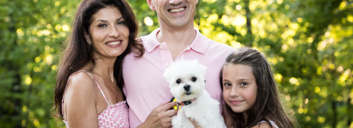 Parents, young girl, and white dog in front of trees during a Forest Park family photo shoot