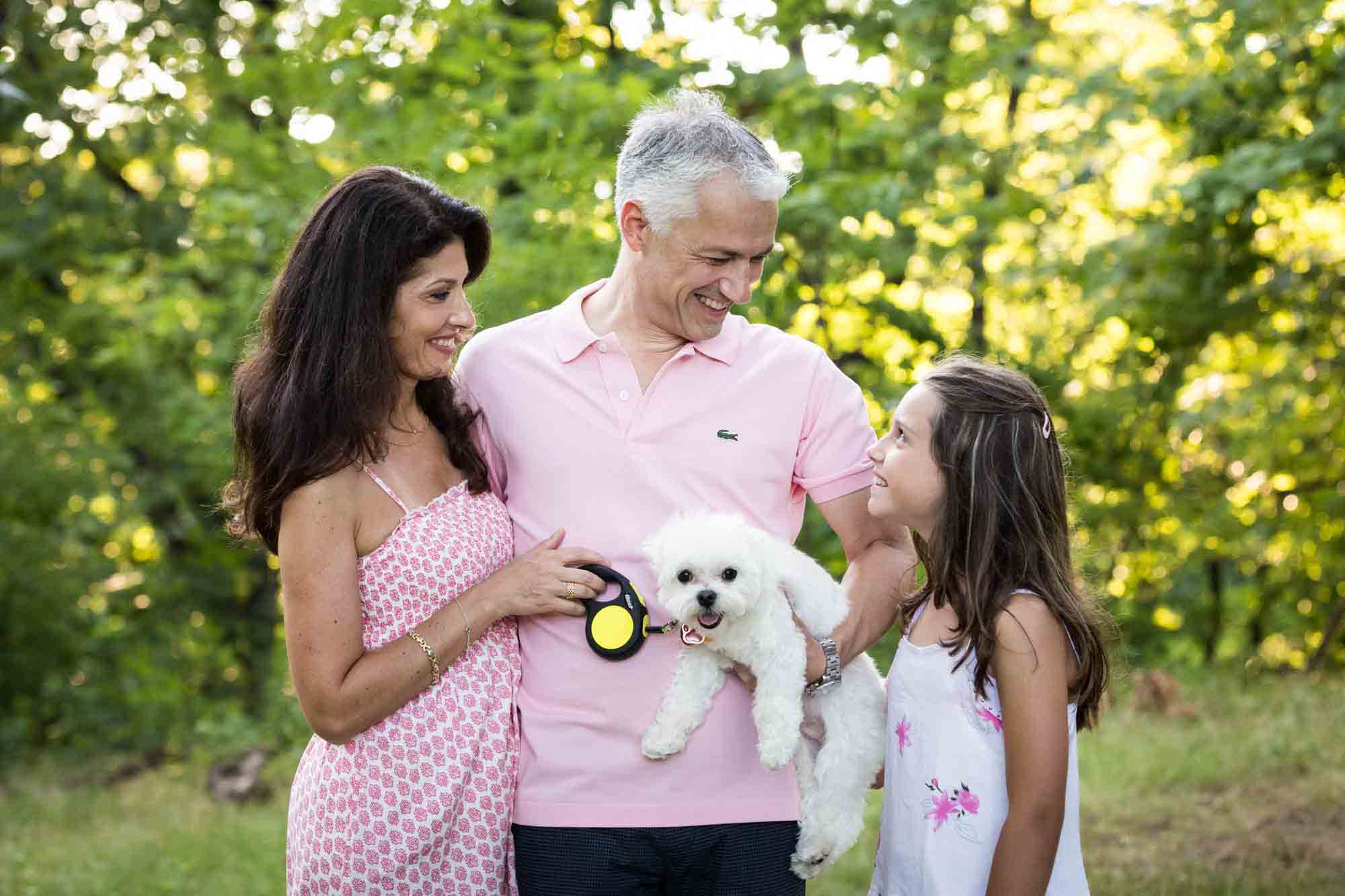 Parents looking down at young girl and small white dog in Forest Park