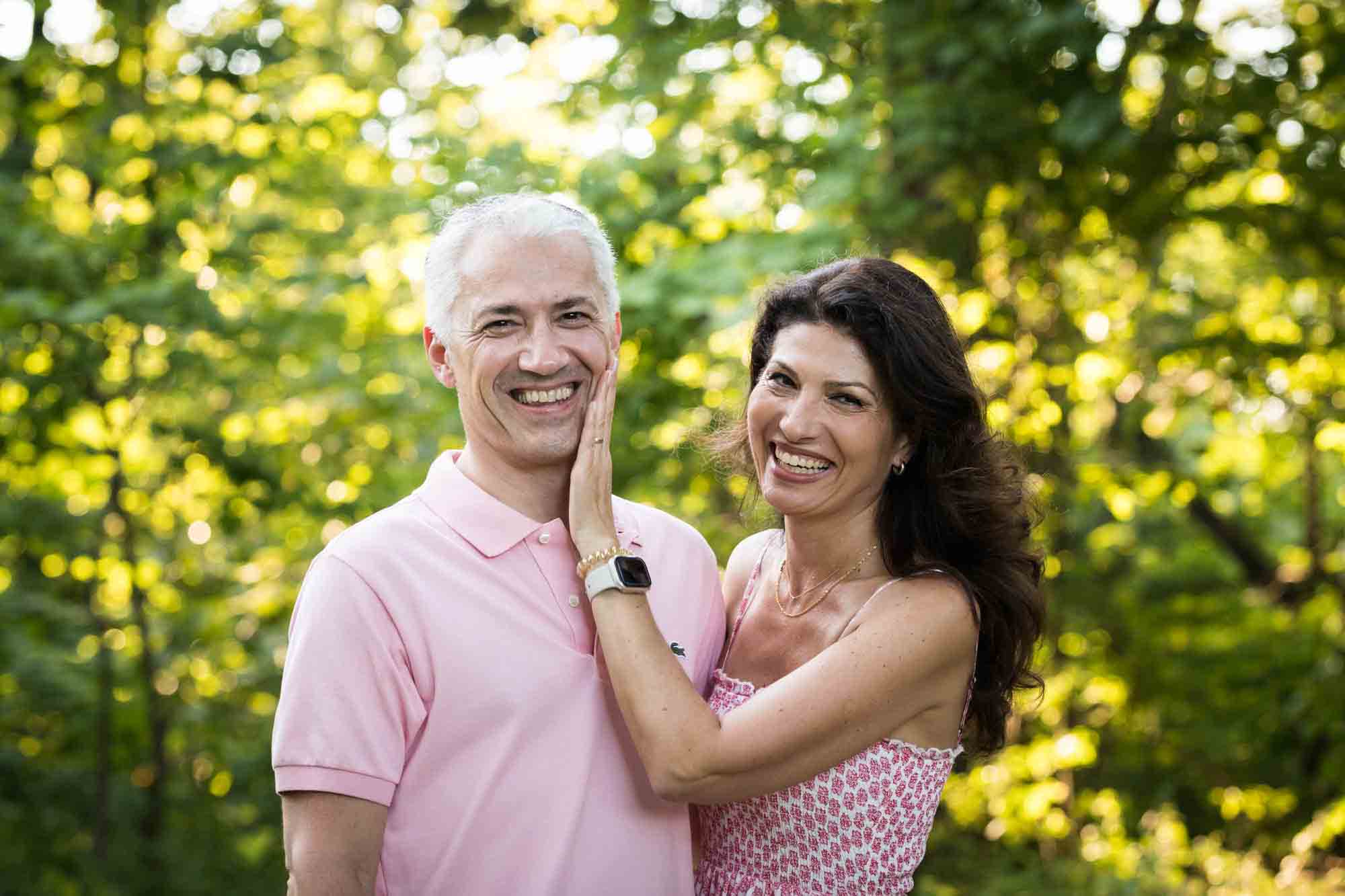 Couple standing in front of trees with woman's hand on man's cheek