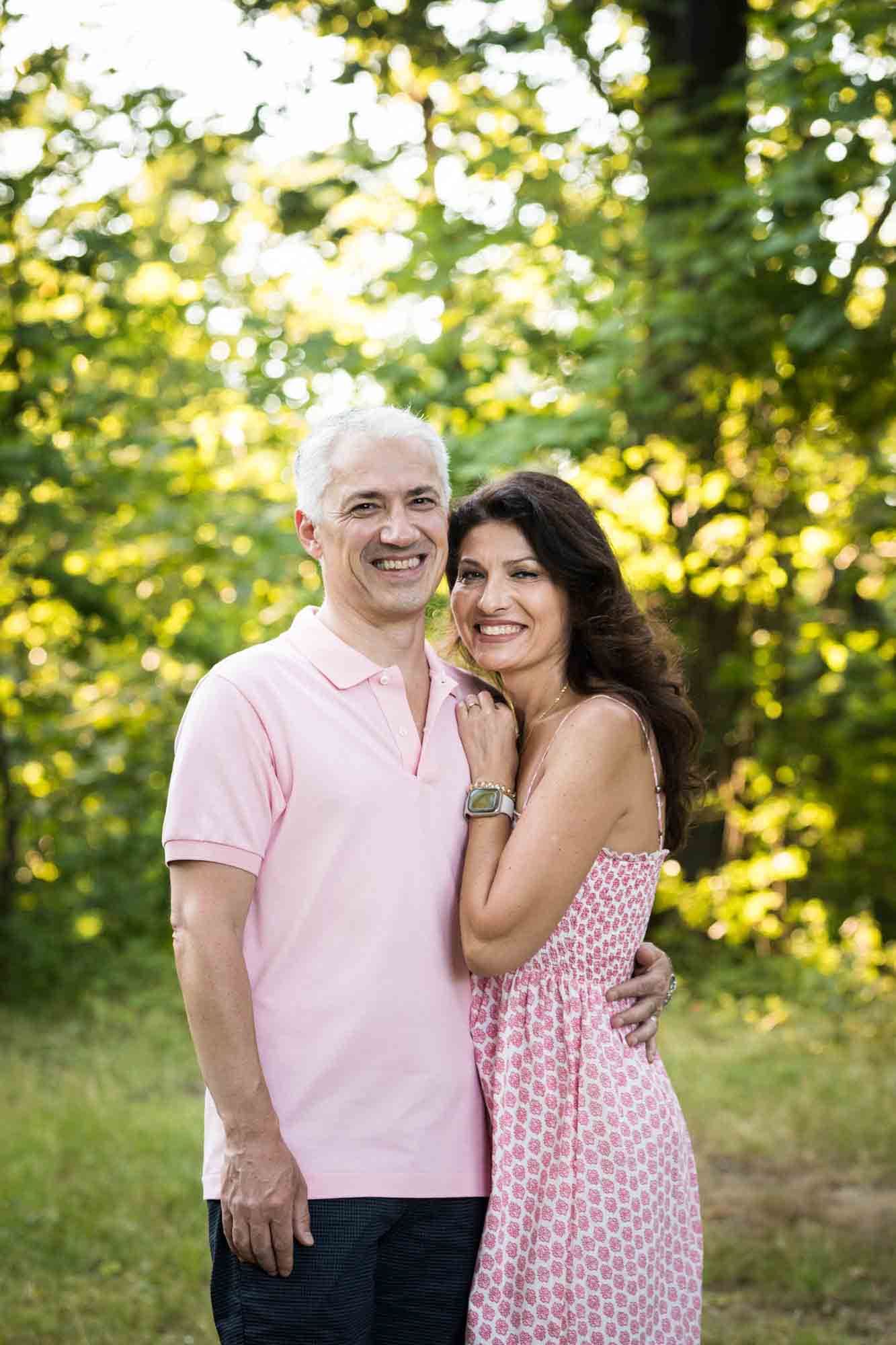 Couple cuddling in front of trees looking into camera during a Forest Park family photo shoot