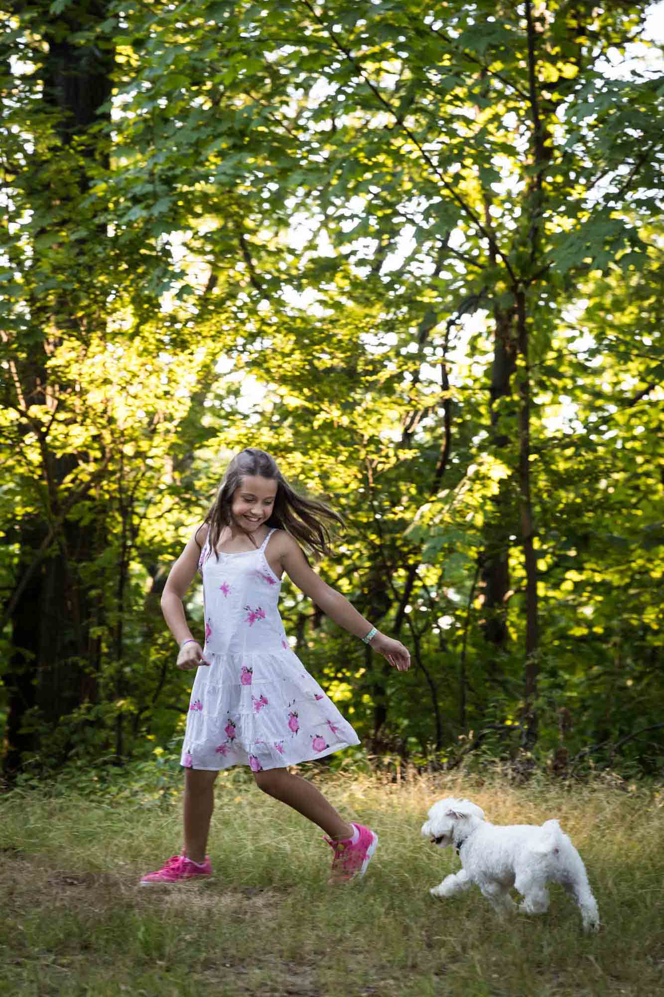 Small white dog chasing girl wearing floral dress during Forest Hills family portrait