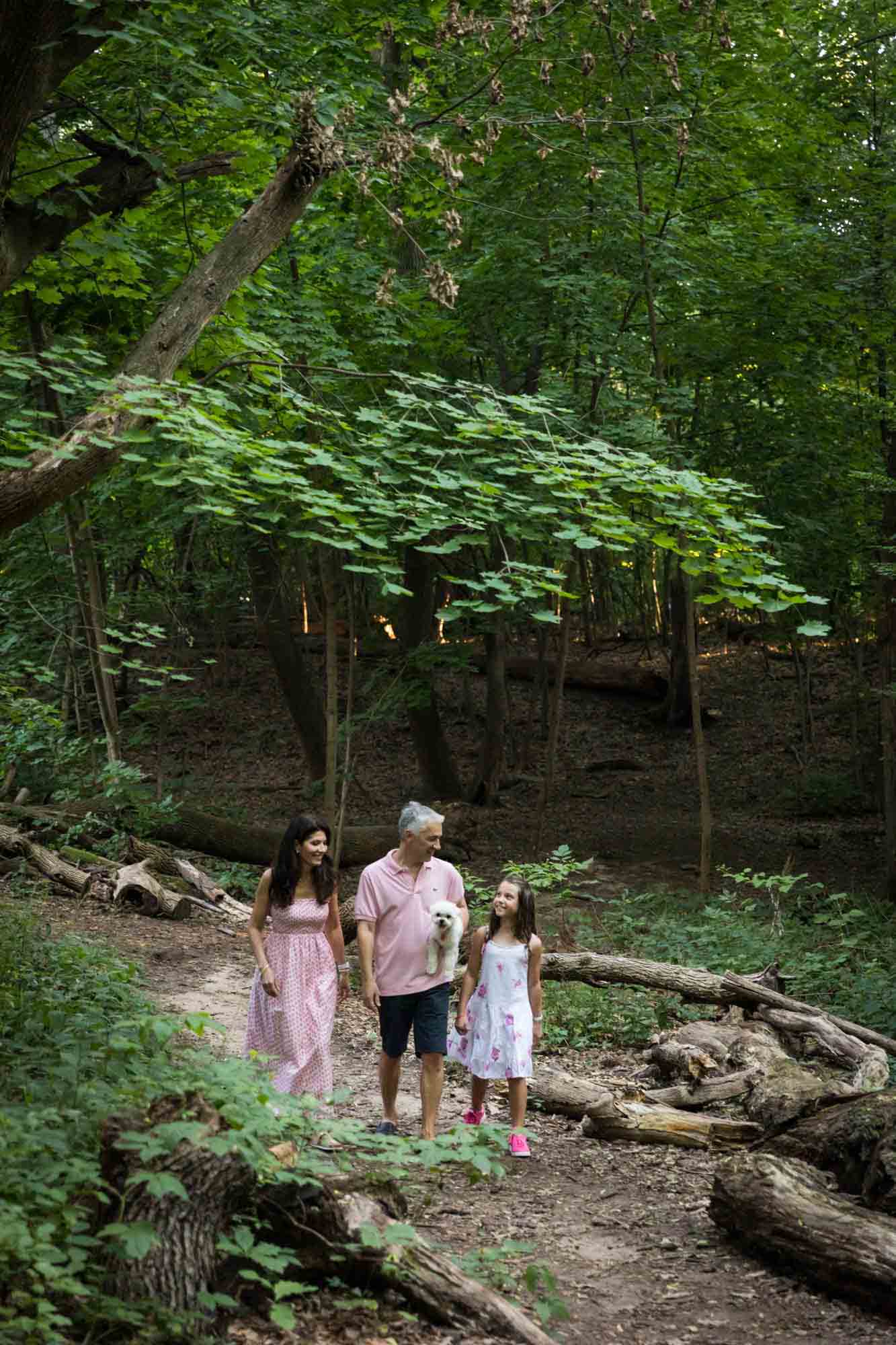 Parents, young girl, and white dog walking along pathway in forest during Forest Hills family portrait