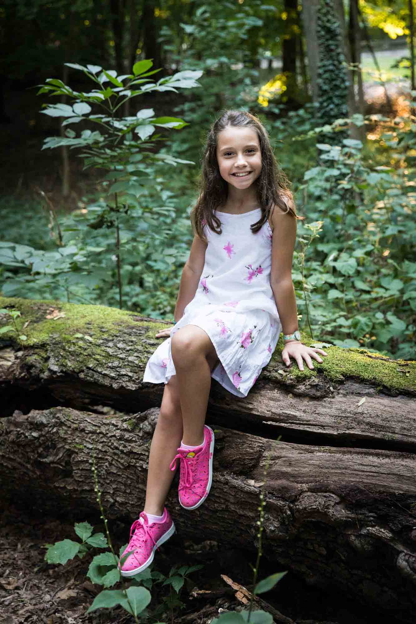 Young girl wearing pink sneakers sitting on moss-covered log during Forest Hills family portrait