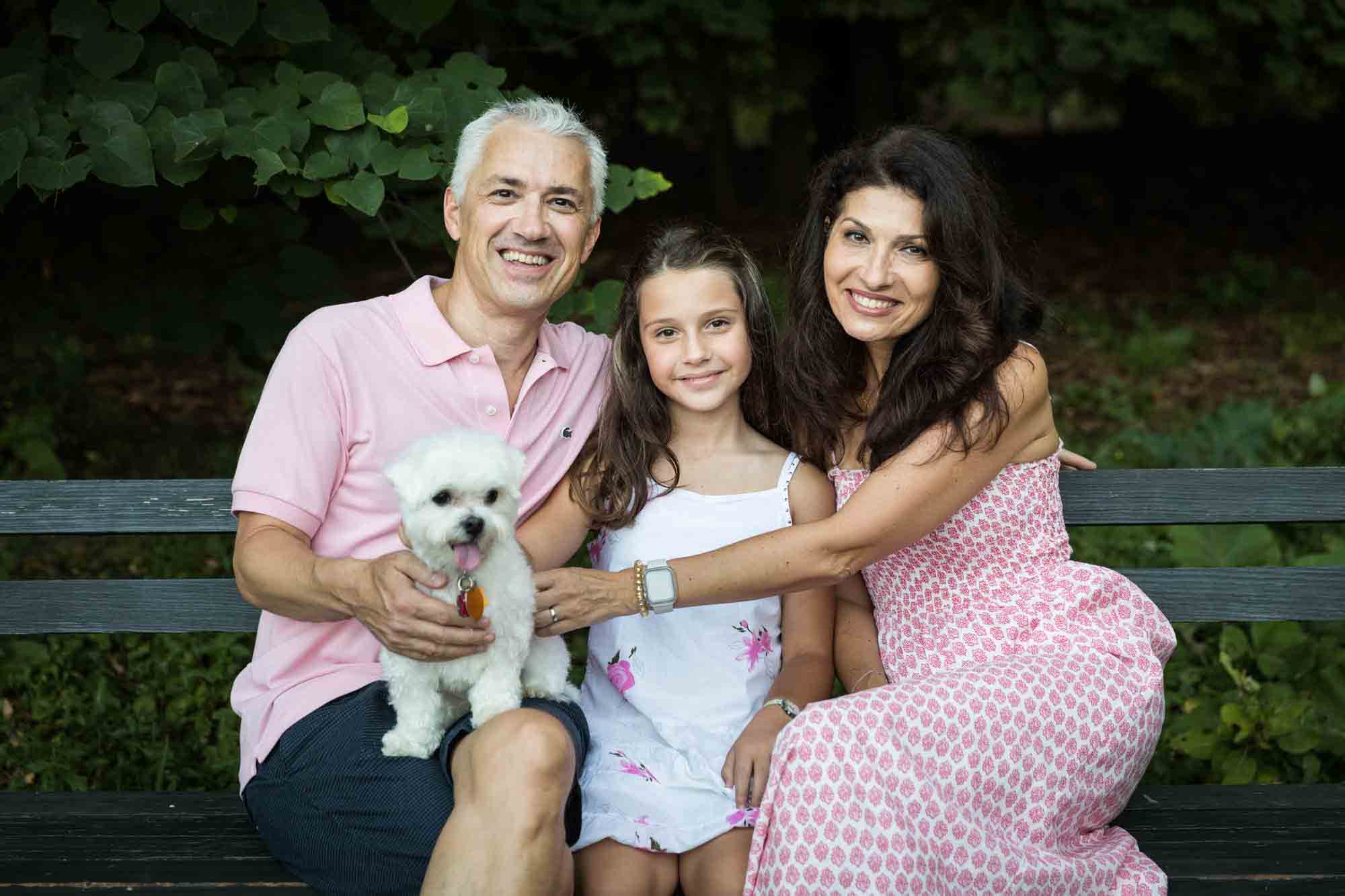 Parents, young girl, and white dog sitting on a bench during a Forest Park family photo shoot