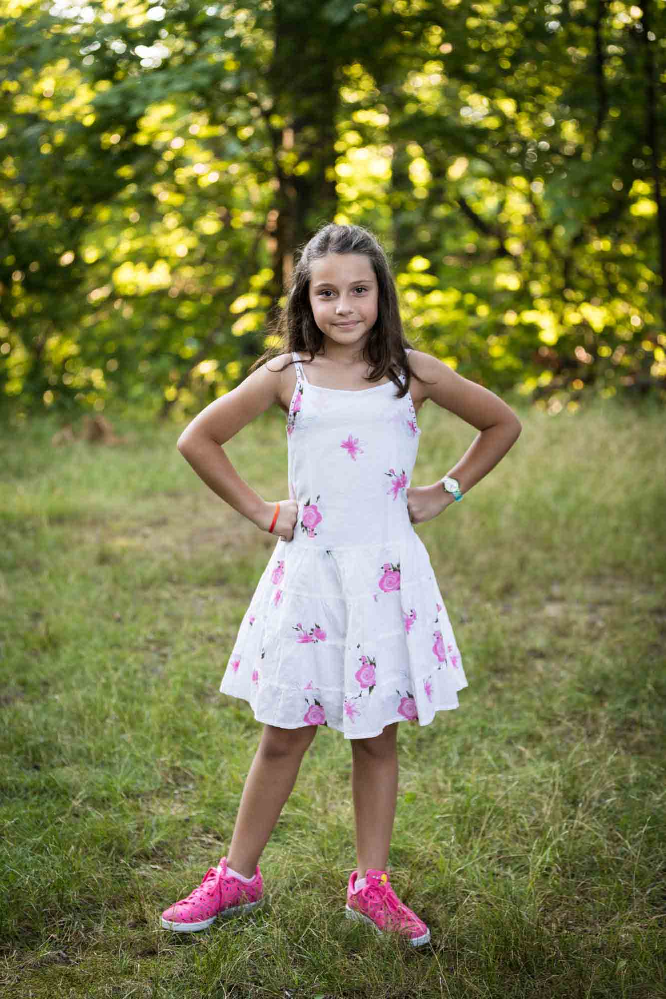 Young girl wearing pink flower dress with hands on hips during a Forest Park family photo shoot