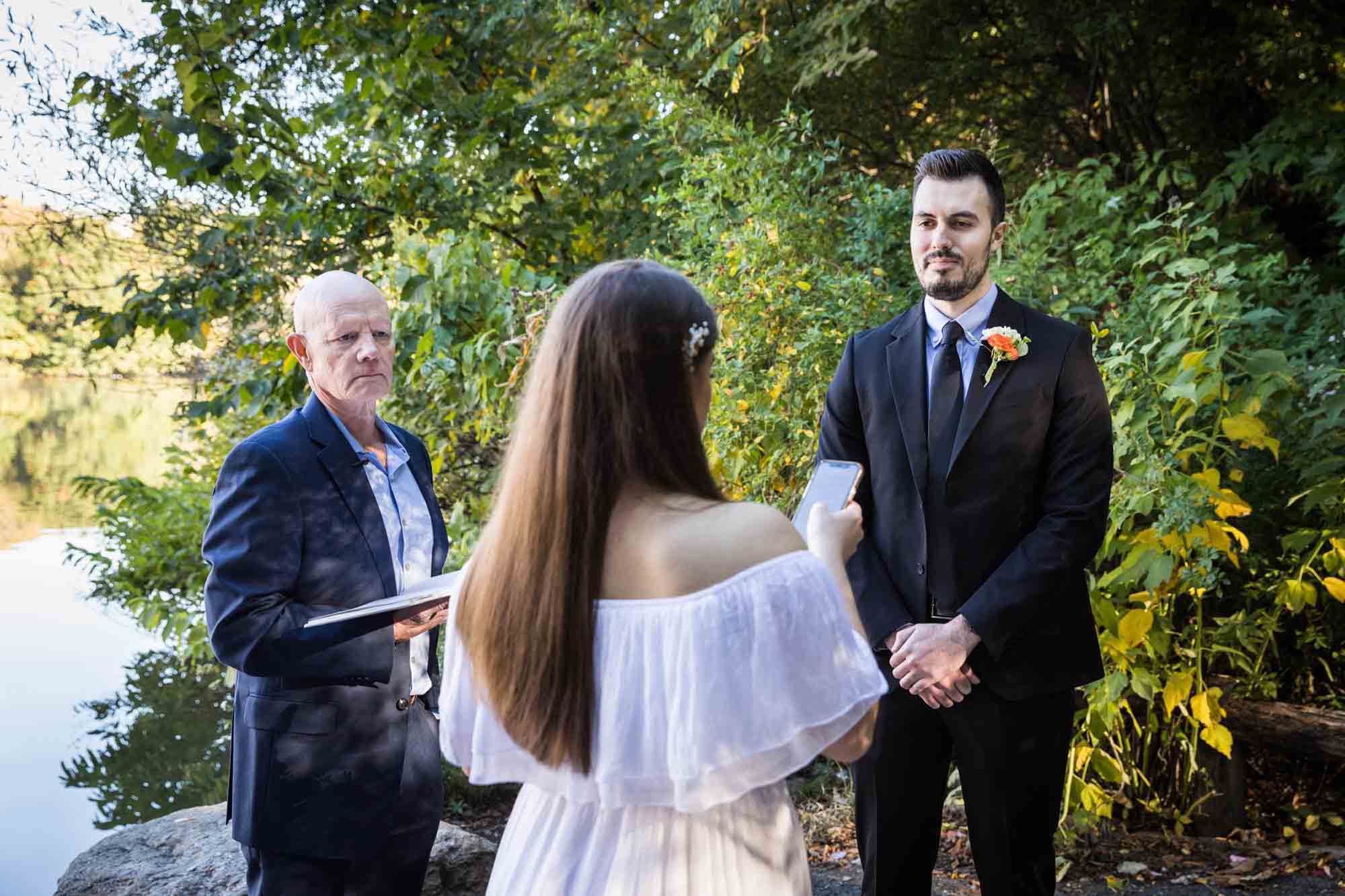 Bride and groom saying vows in front of officiant Article on how to elope in Central Park by NYC wedding photojournalist, Kelly Williams. Includes photos from a real wedding near Bow Bridge.