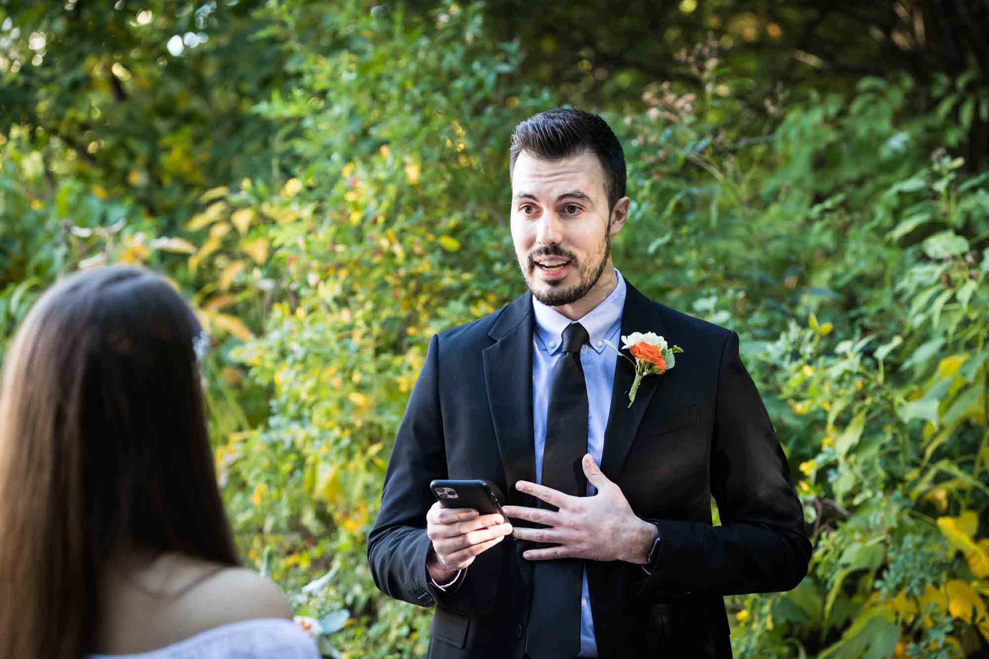 Groom holding cell phone and saying vows at Central Park elopement