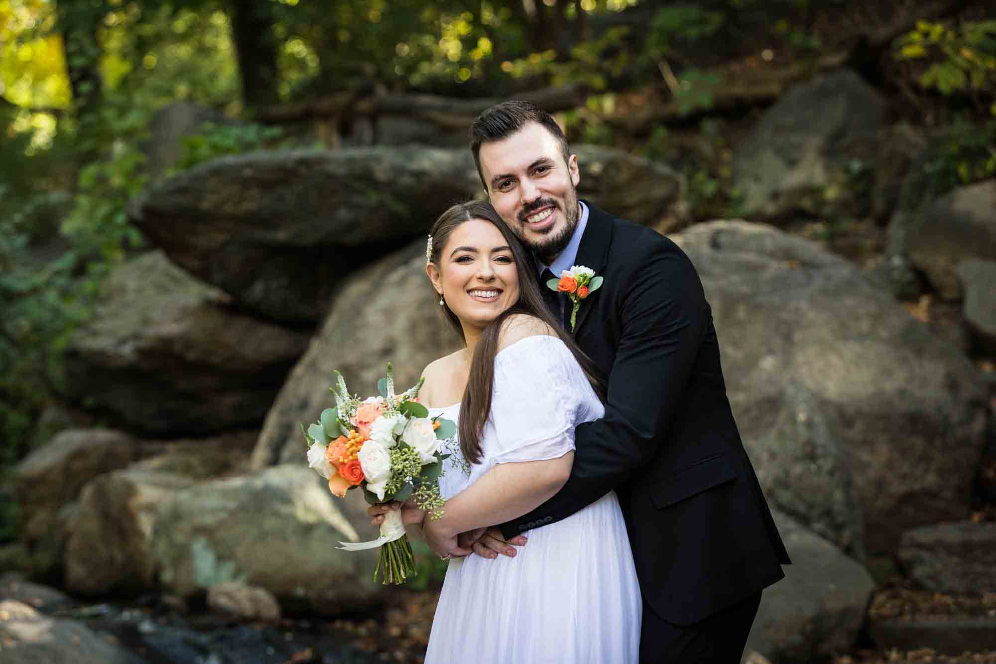 Bride and groom hugging in front of rocks in forest after Central Park elopement