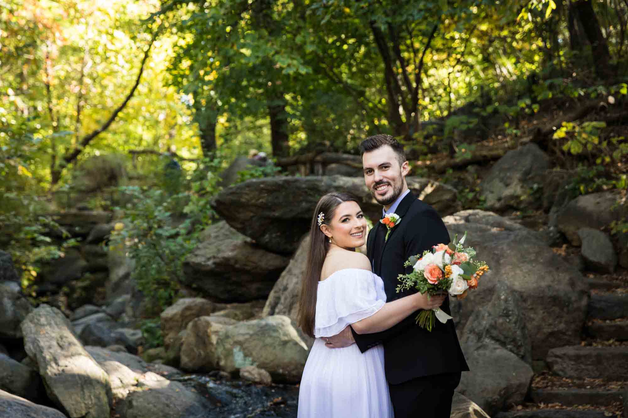 Bride and groom hugging in front of rocks in forest after Central Park elopement