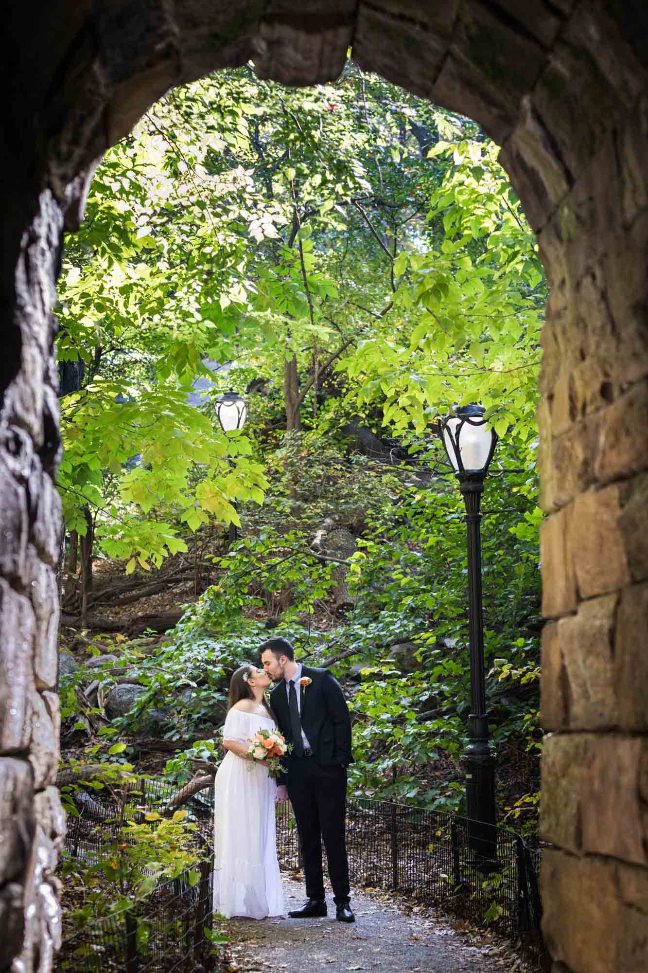 Bride and groom kissing under stone arch Article on how to elope in Central Park by NYC wedding photojournalist, Kelly Williams. Includes photos from a real wedding near Bow Bridge.