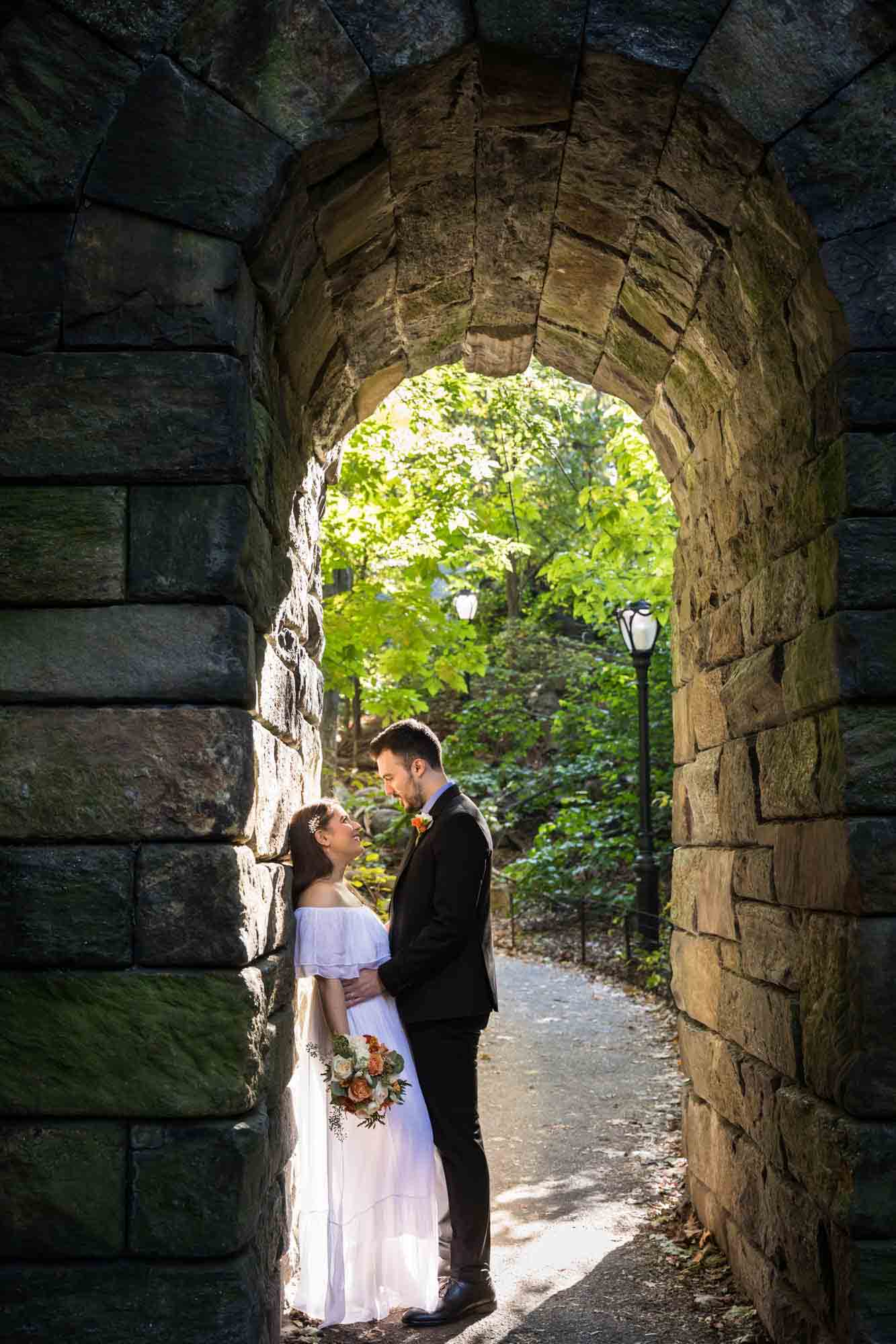 Bride and groom kissing under stone arch Article on how to elope in Central Park by NYC wedding photojournalist, Kelly Williams. Includes photos from a real wedding near Bow Bridge.