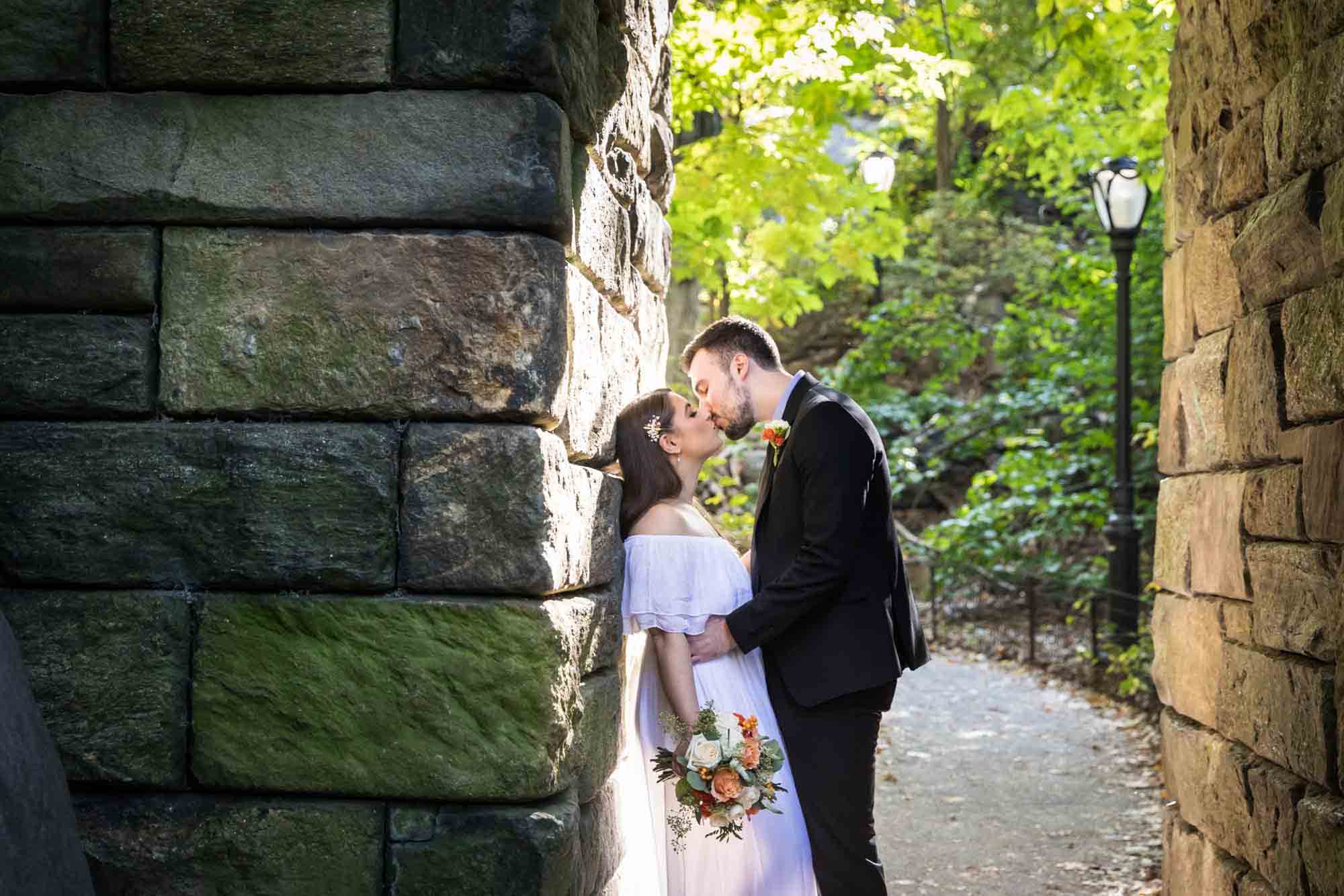 Bride and groom kissing under stone arch Article on how to elope in Central Park by NYC wedding photojournalist, Kelly Williams. Includes photos from a real wedding near Bow Bridge.
