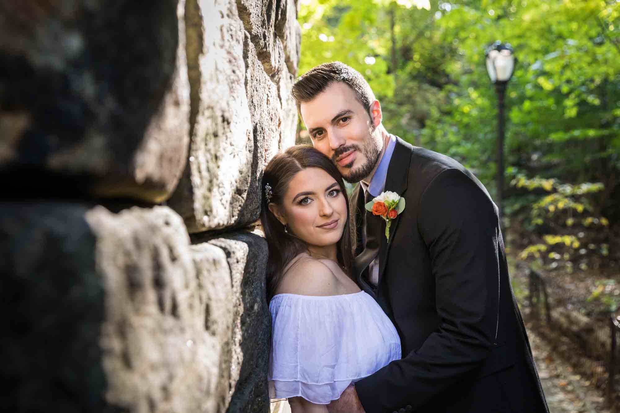 Couple hugging against stone wall for article on how to elope in Central Park