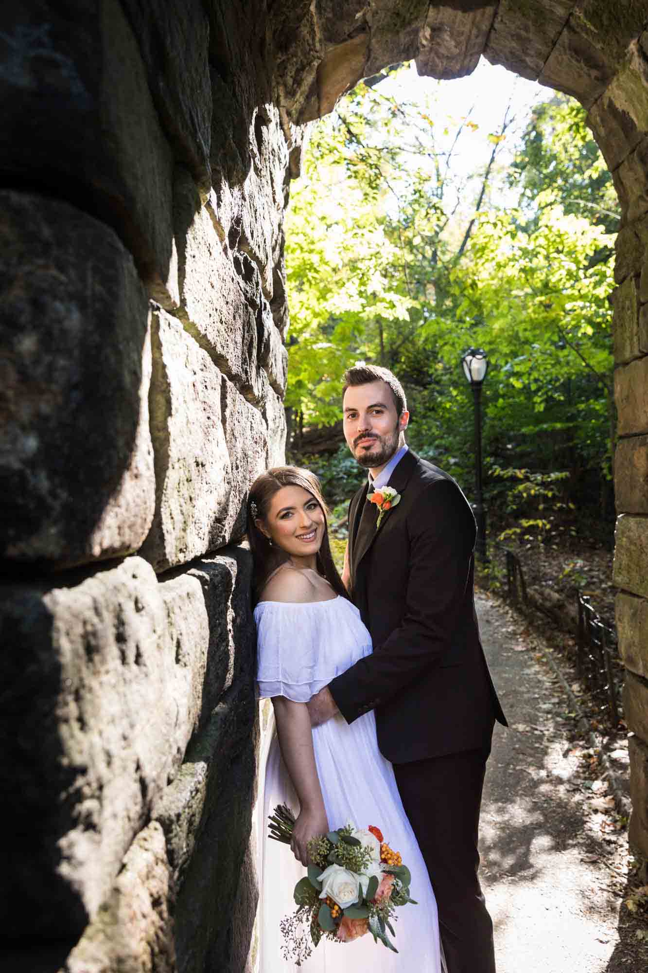 Couple hugging against stone wall for article on how to elope in Central Park