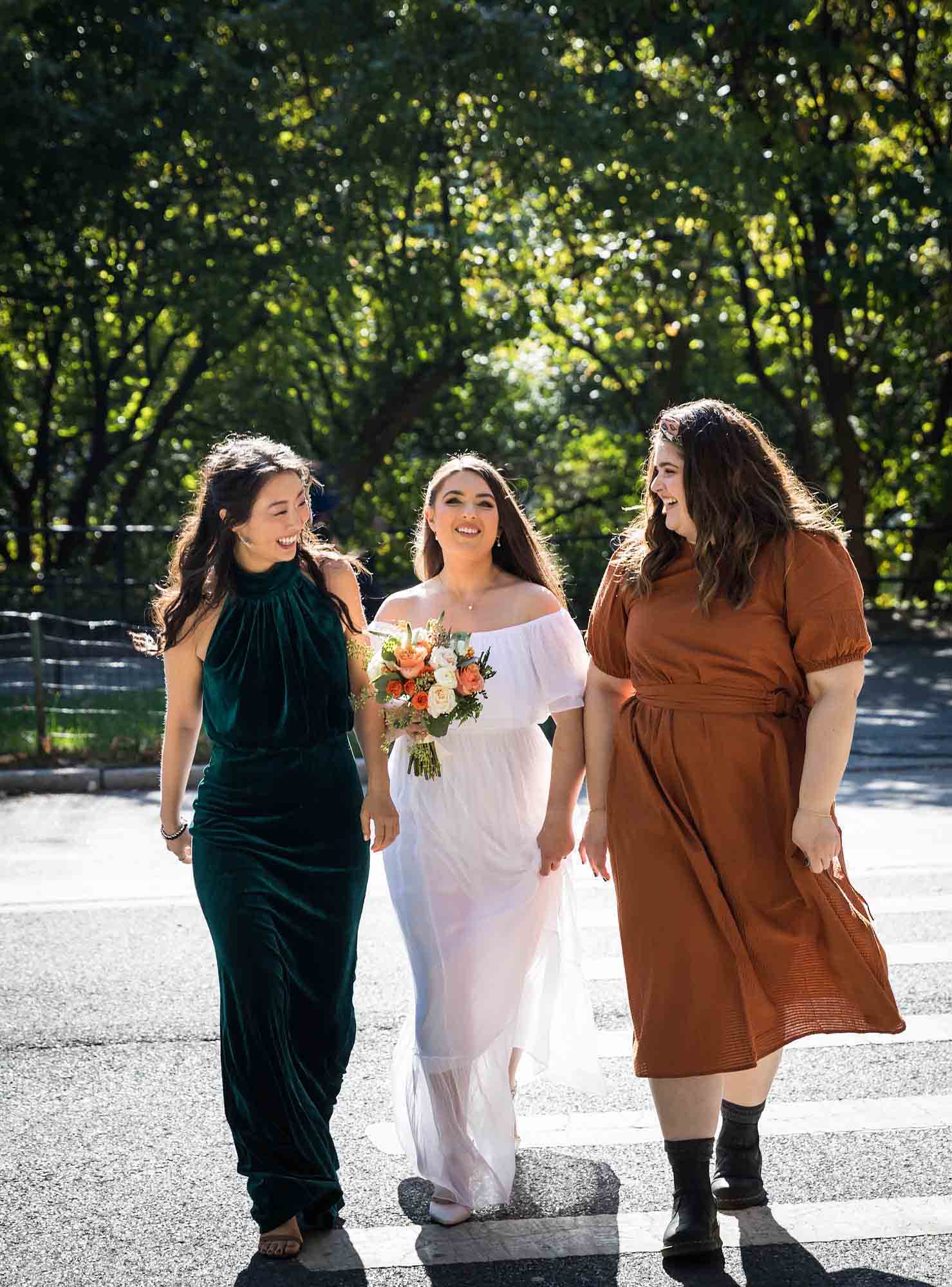 Bride walking between two female friends Article on how to elope in Central Park by NYC wedding photojournalist, Kelly Williams. Includes photos from a real wedding near Bow Bridge.